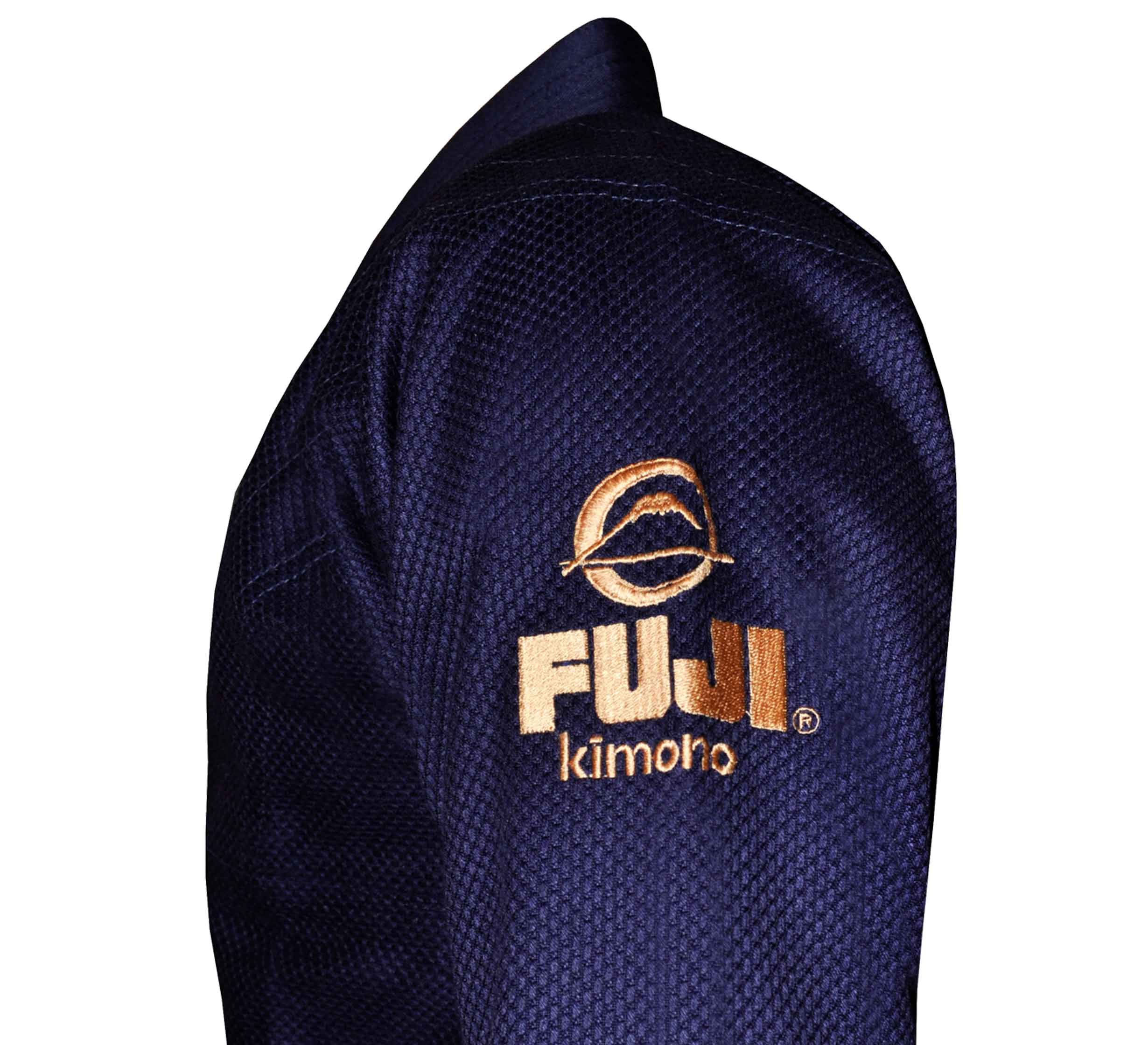 A close-up of the sleeve of a dark blue textured All Around BJJ Gi with a gold embroidered logo and FUJI Kimono text on the upper arm.