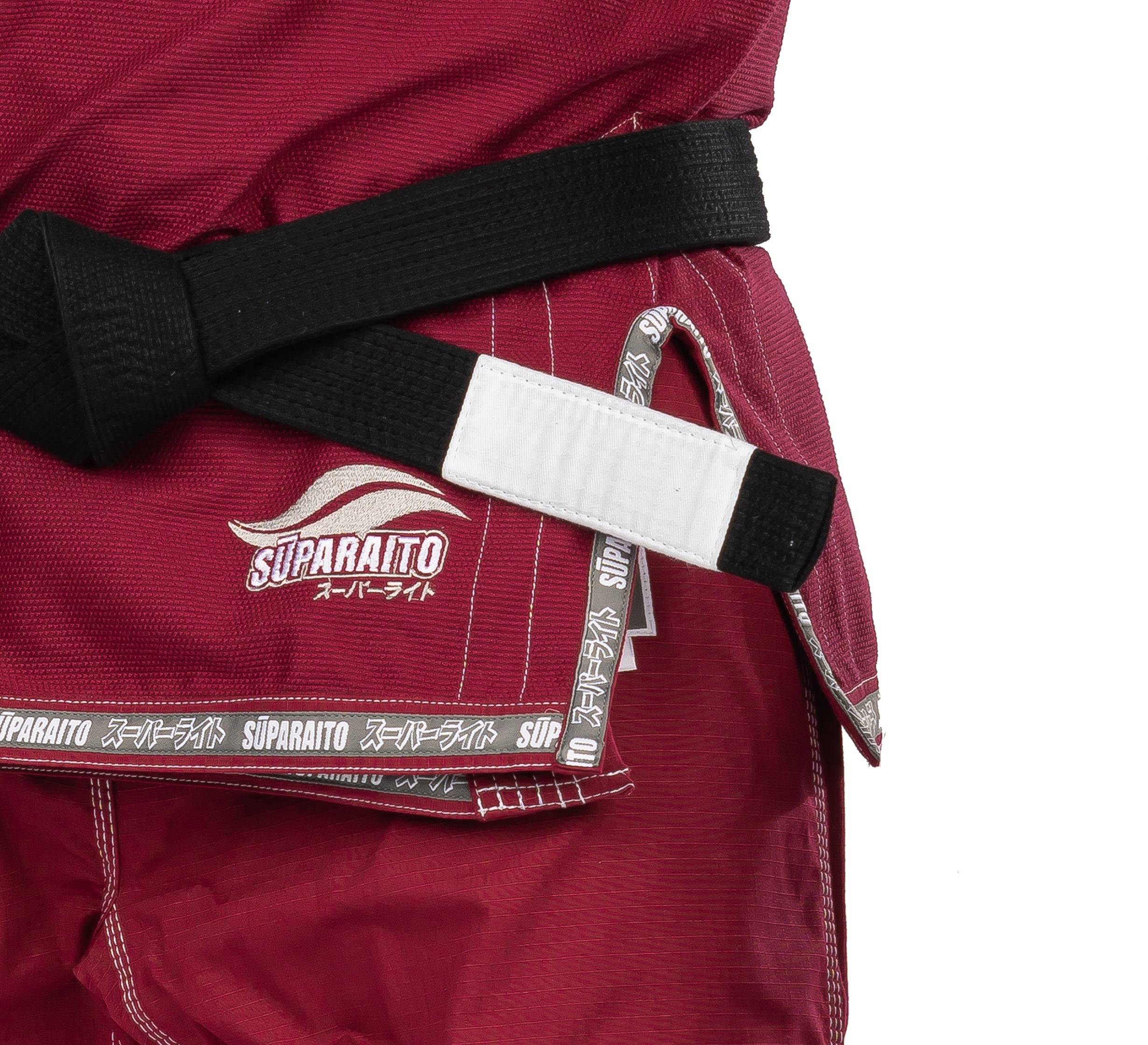 A close-up of the Suparaito BJJ Gi Burgundy, featuring white Suparaito branding, a black belt at the waist, and hem and tags with Japanese characters and the brand name.