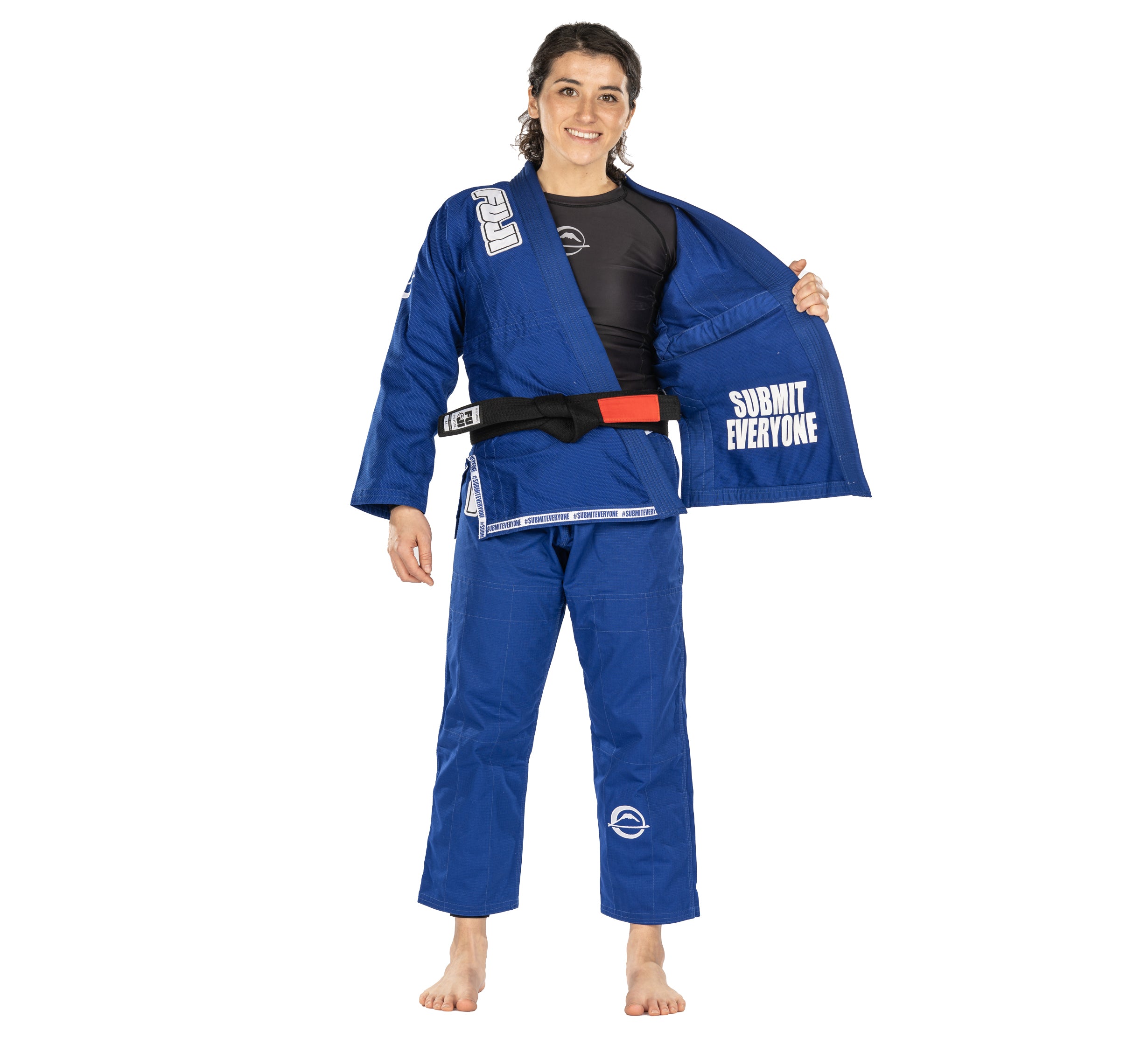 Wearing the Submit Everyone Womens BJJ Gi Blue, a barefoot woman with a black belt smiles and opens her jacket to show "SUBMIT EVERYONE" printed inside.