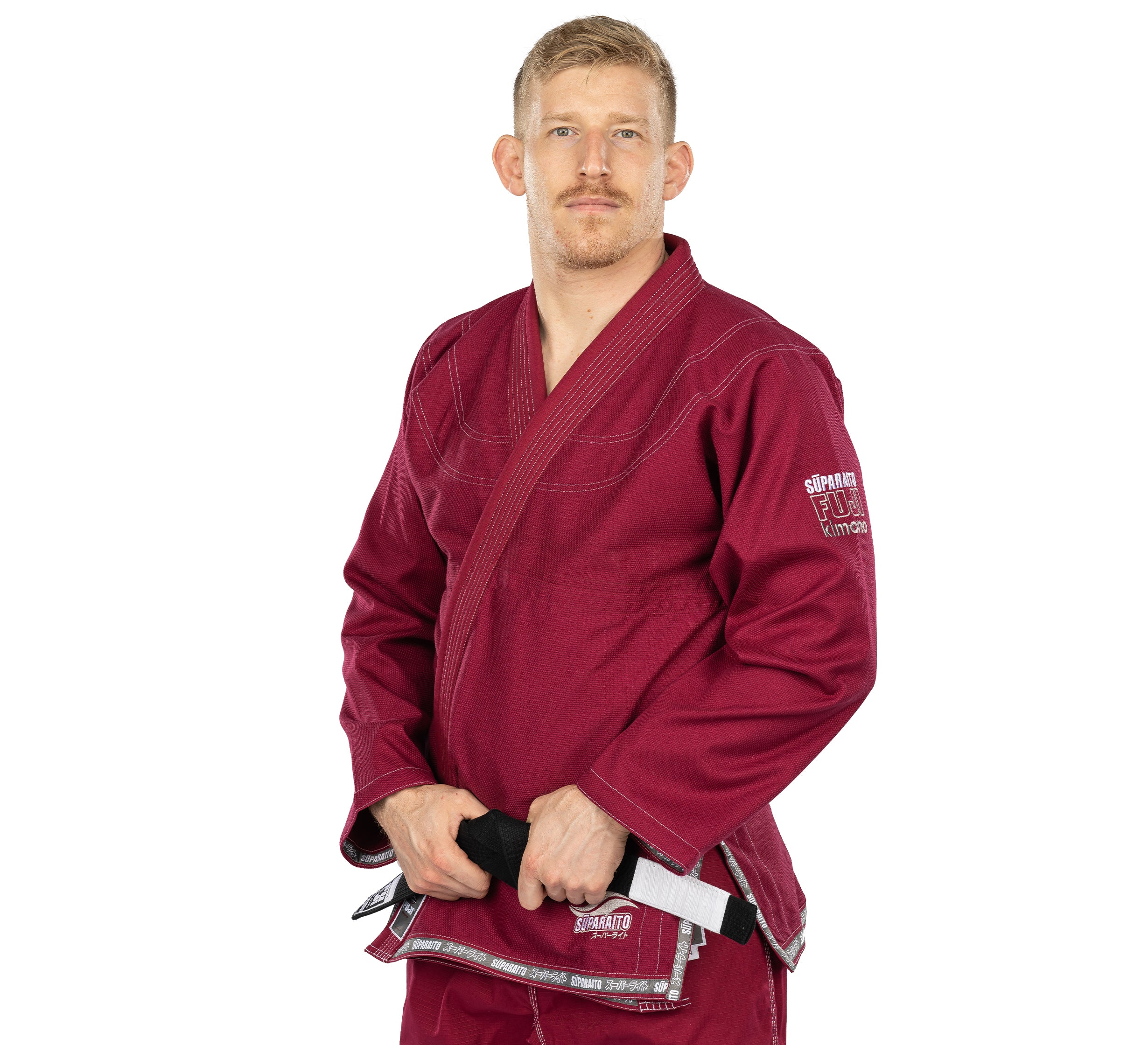 A man with short blond hair and a mustache stands facing forward, wearing the Suparaito BJJ Gi Burgundy and holding a black belt.