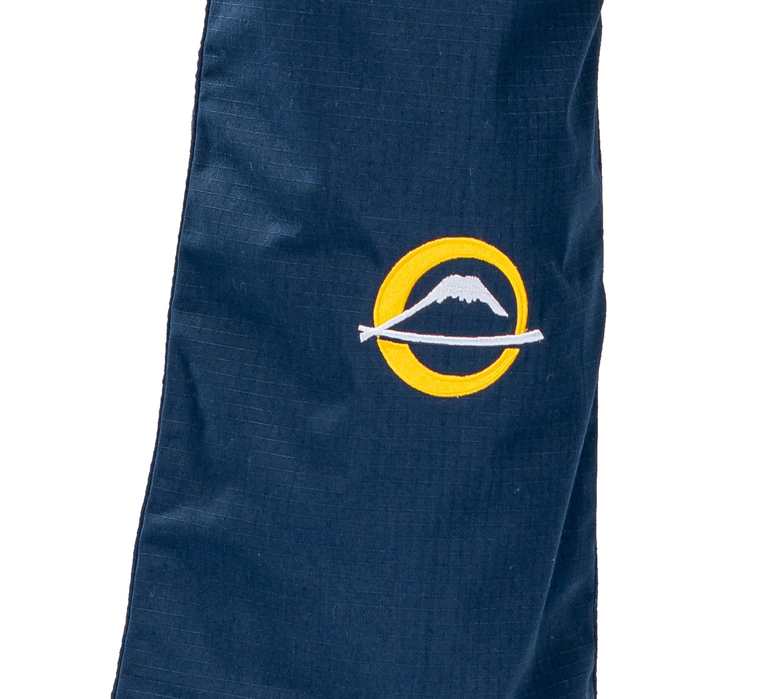 A close-up of the Suparaito BJJ Gi Worldwide Edition Navy shows its navy fabric with an embroidered yellow circle featuring a white mountain and stick design.