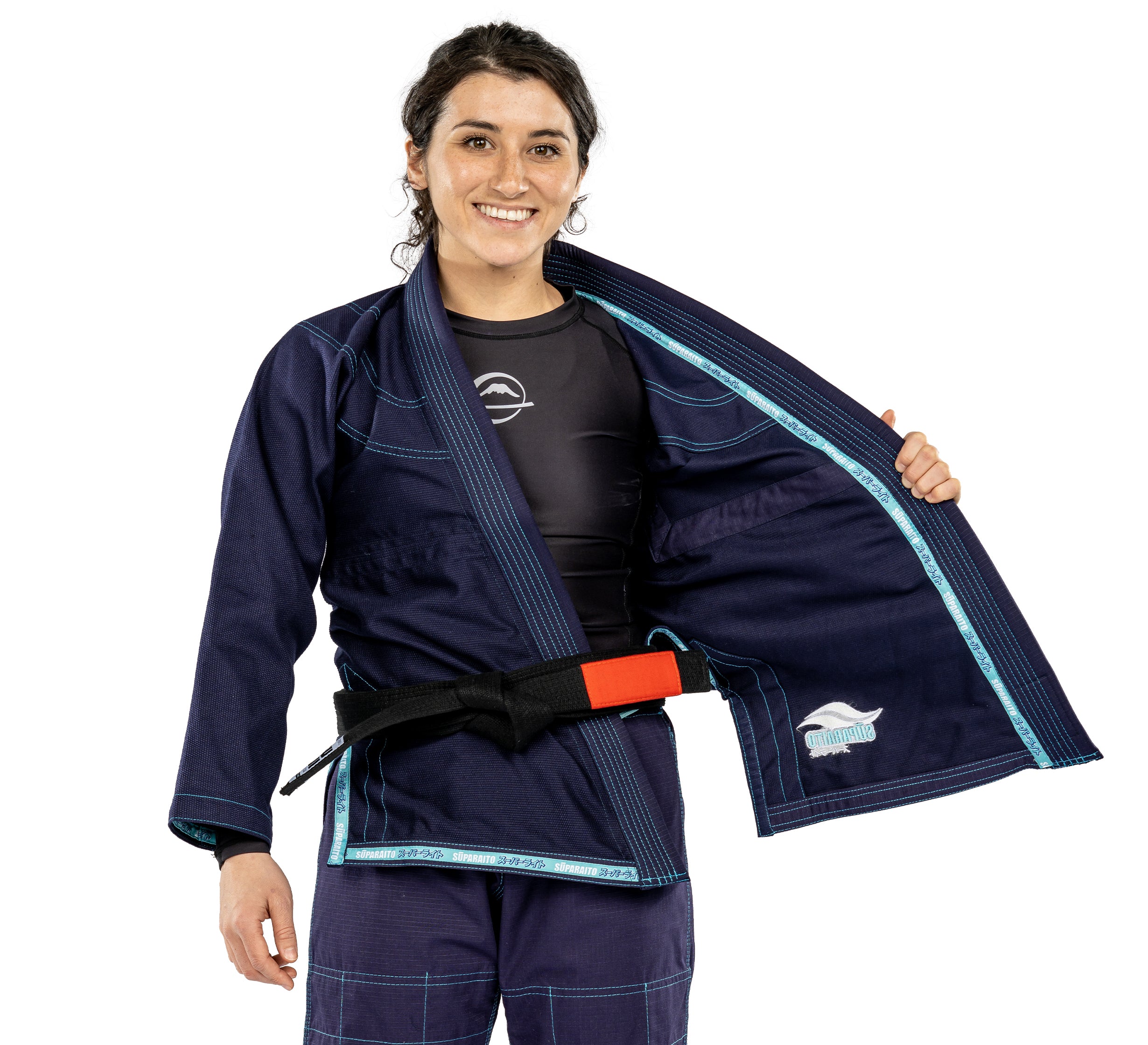 A smiling woman in the Suparaito Womens BJJ Gi Navy and a black belt with red bar holds open her jacket to display the inside lining.