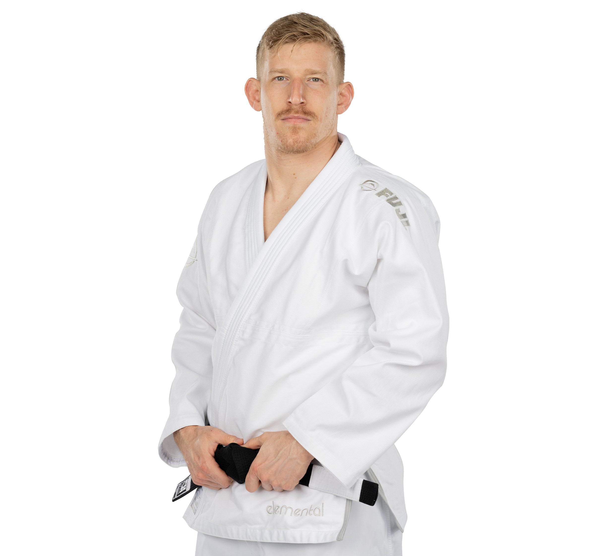 A man with short blond hair and a trimmed beard wears the Elemental BJJ Gi White and holds a black belt, standing against a plain white background.