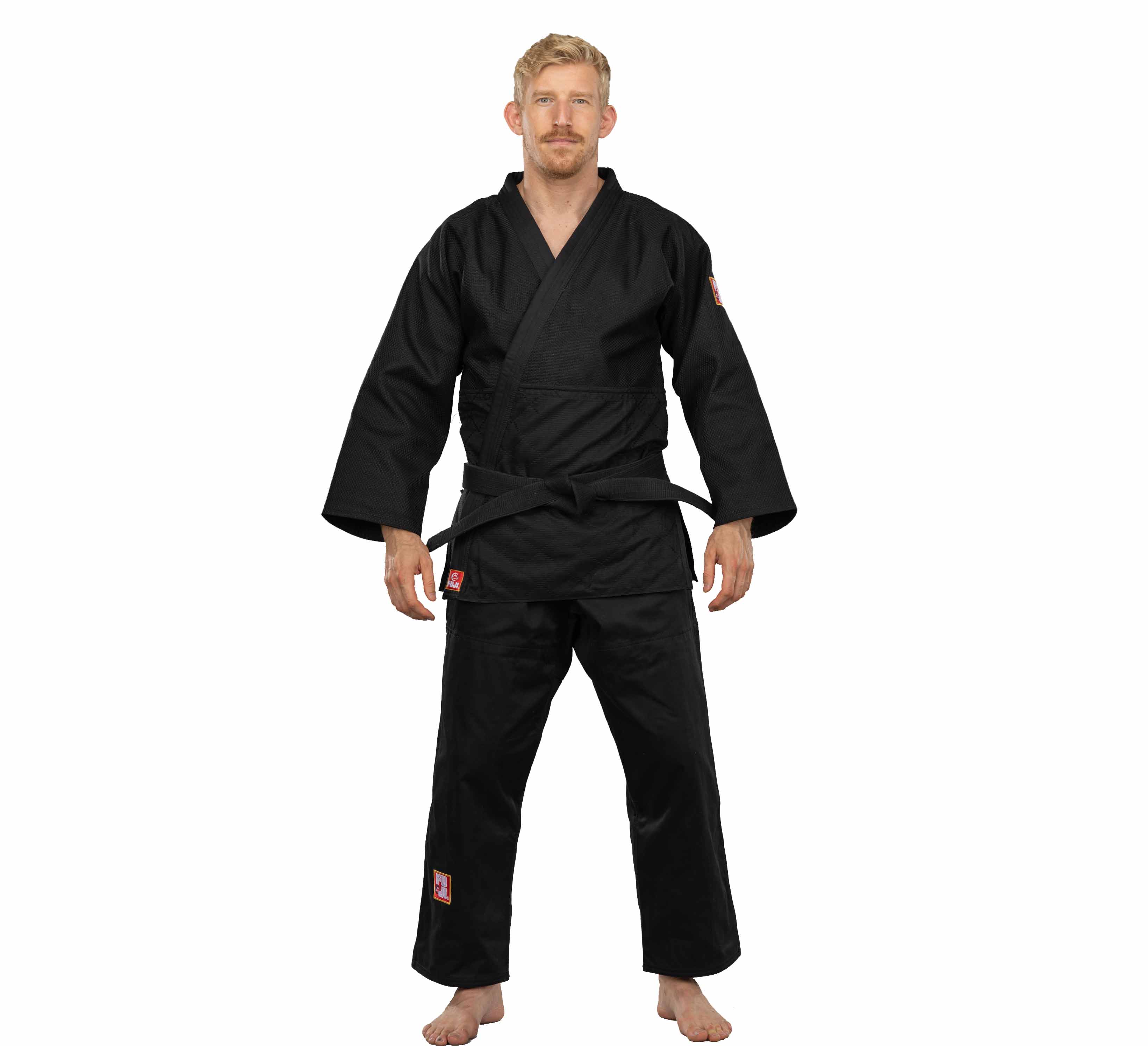 A man with blonde hair and a trimmed beard stands barefoot, facing forward against a plain white background, wearing the Euro Competition Judo Gi Black with a black belt.