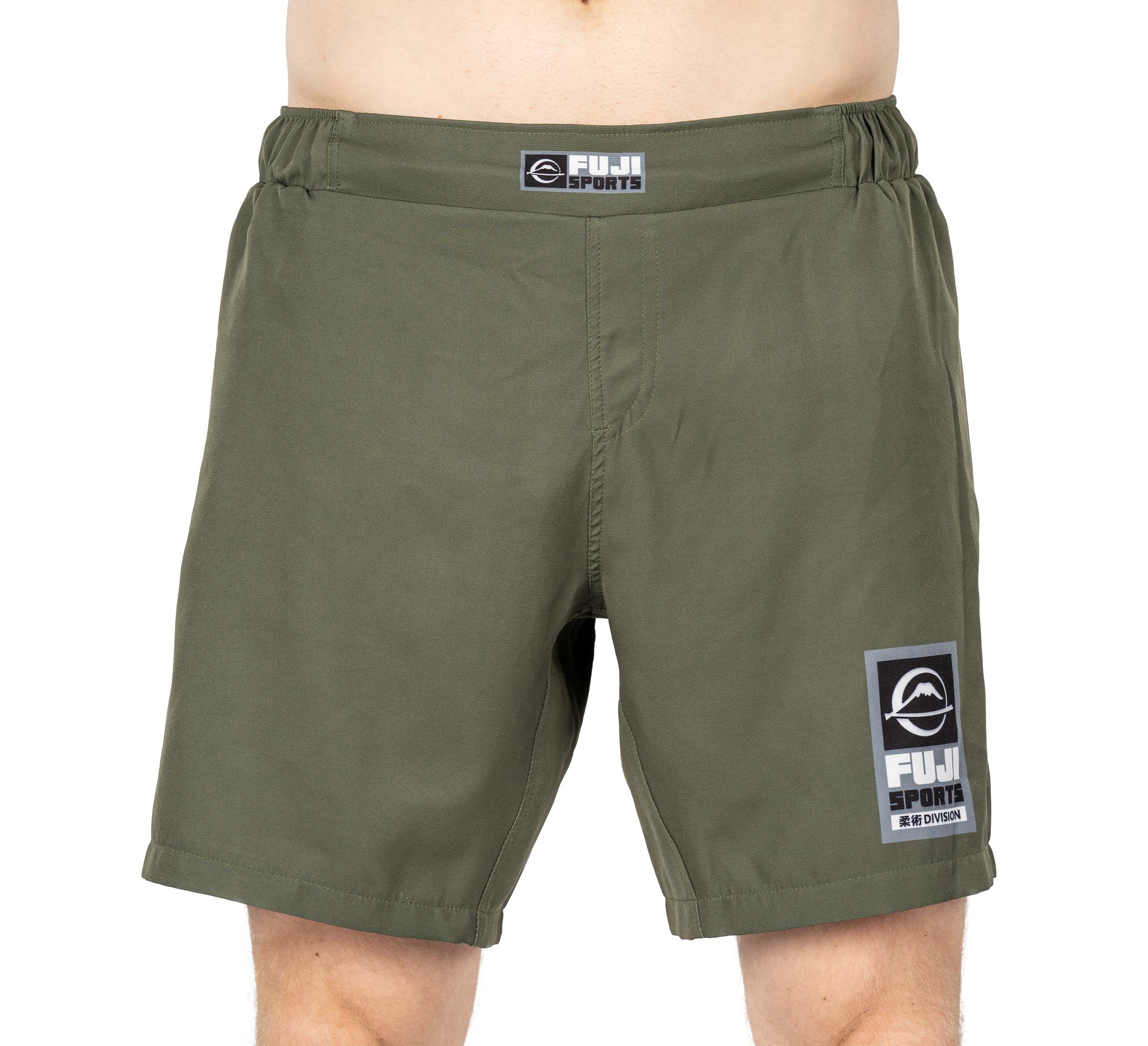 A person wearing Ultimate Grappling Shorts Military Green by FUJI Sports, featuring an elastic waistband and a FUJI Sports logo patch on the left leg. These comfortable shorts are perfect for athletic or casual wear.
