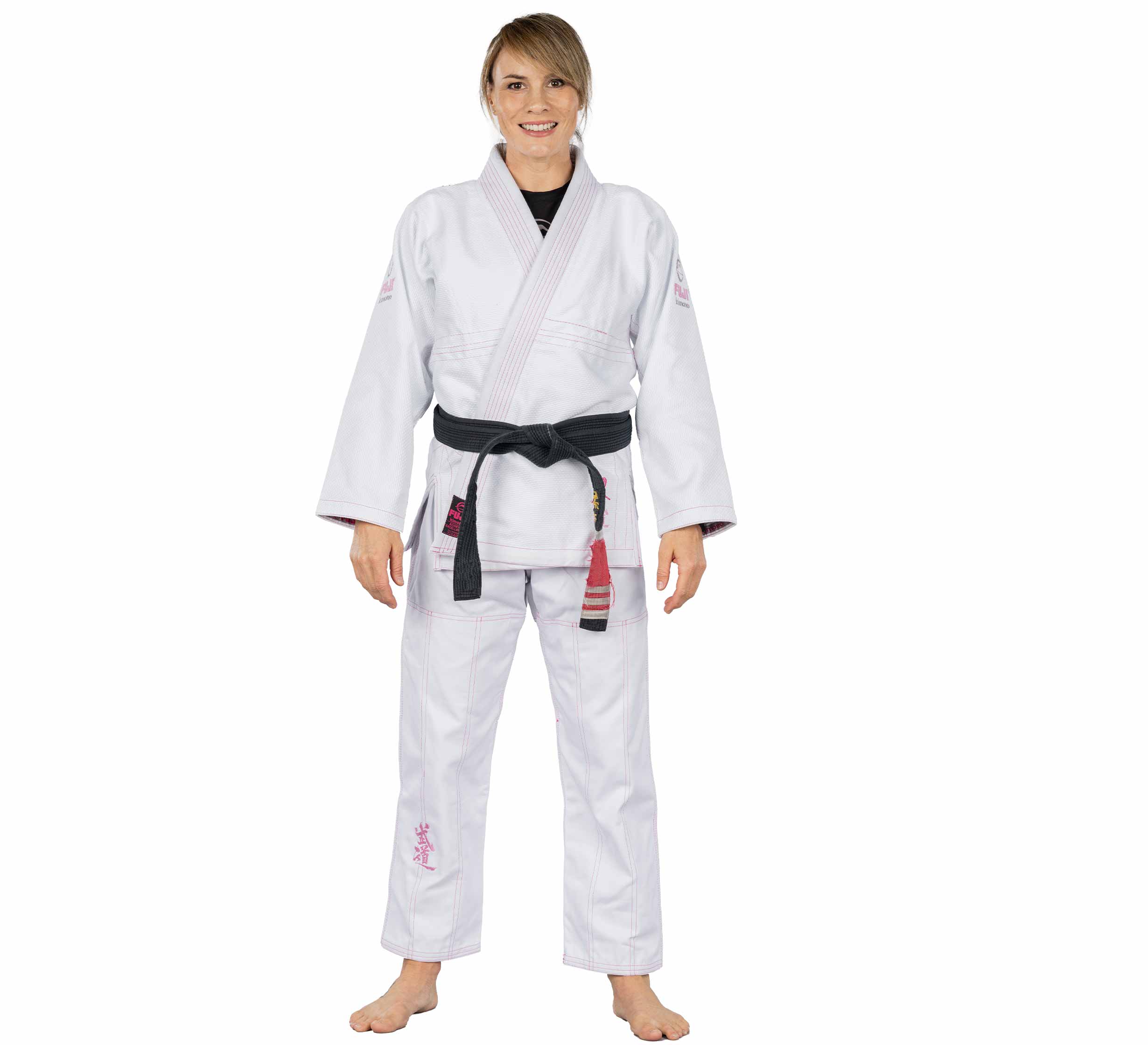 A woman wearing the Blossom Womens Jiu Jitsu Gi White and a black belt stands barefoot on a white background, smiling and facing forward.