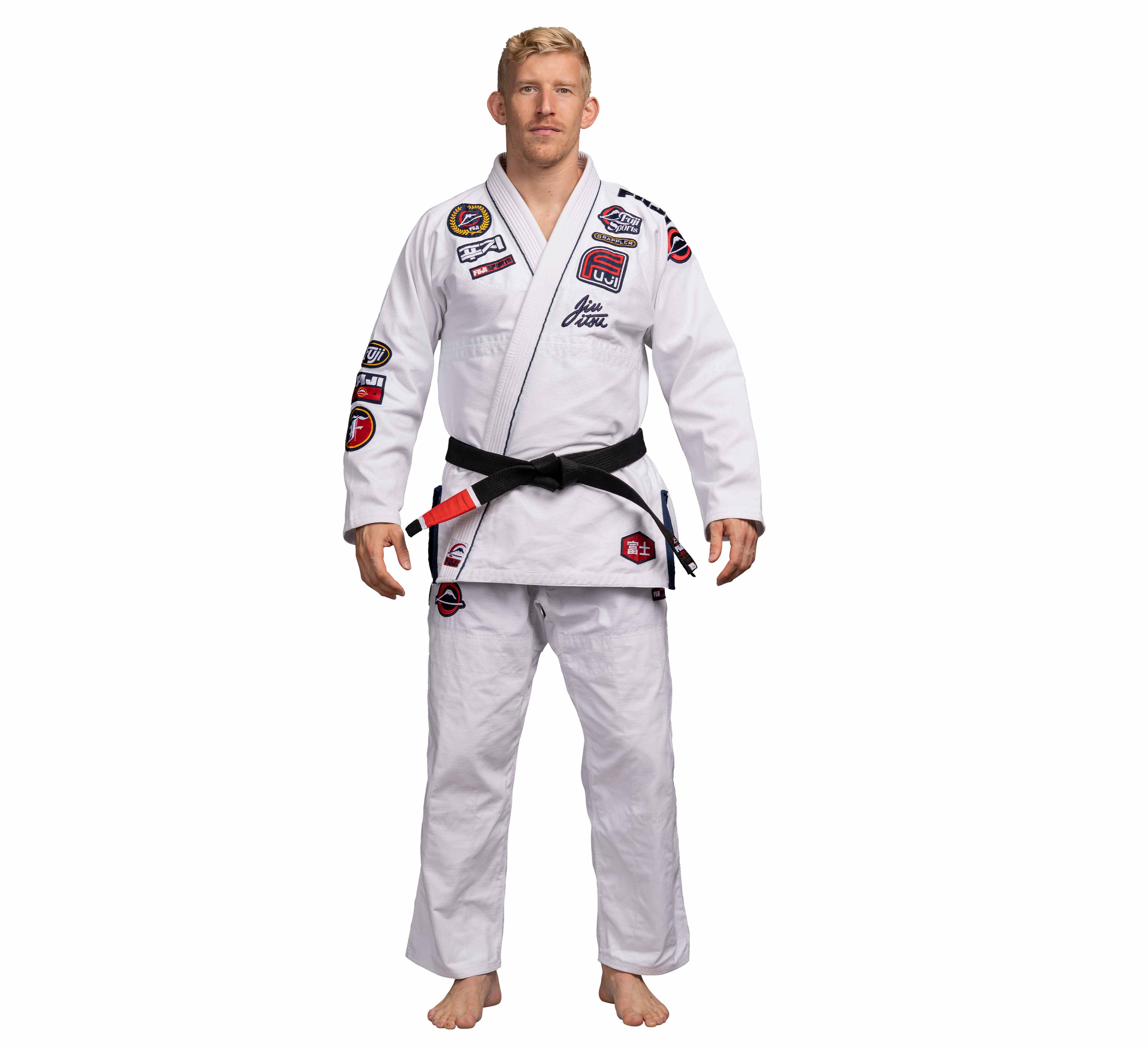 A man stands barefoot against a plain white background, wearing the Suparaito BJJ Gi XTR Edition White adorned with multiple patches and a black belt.