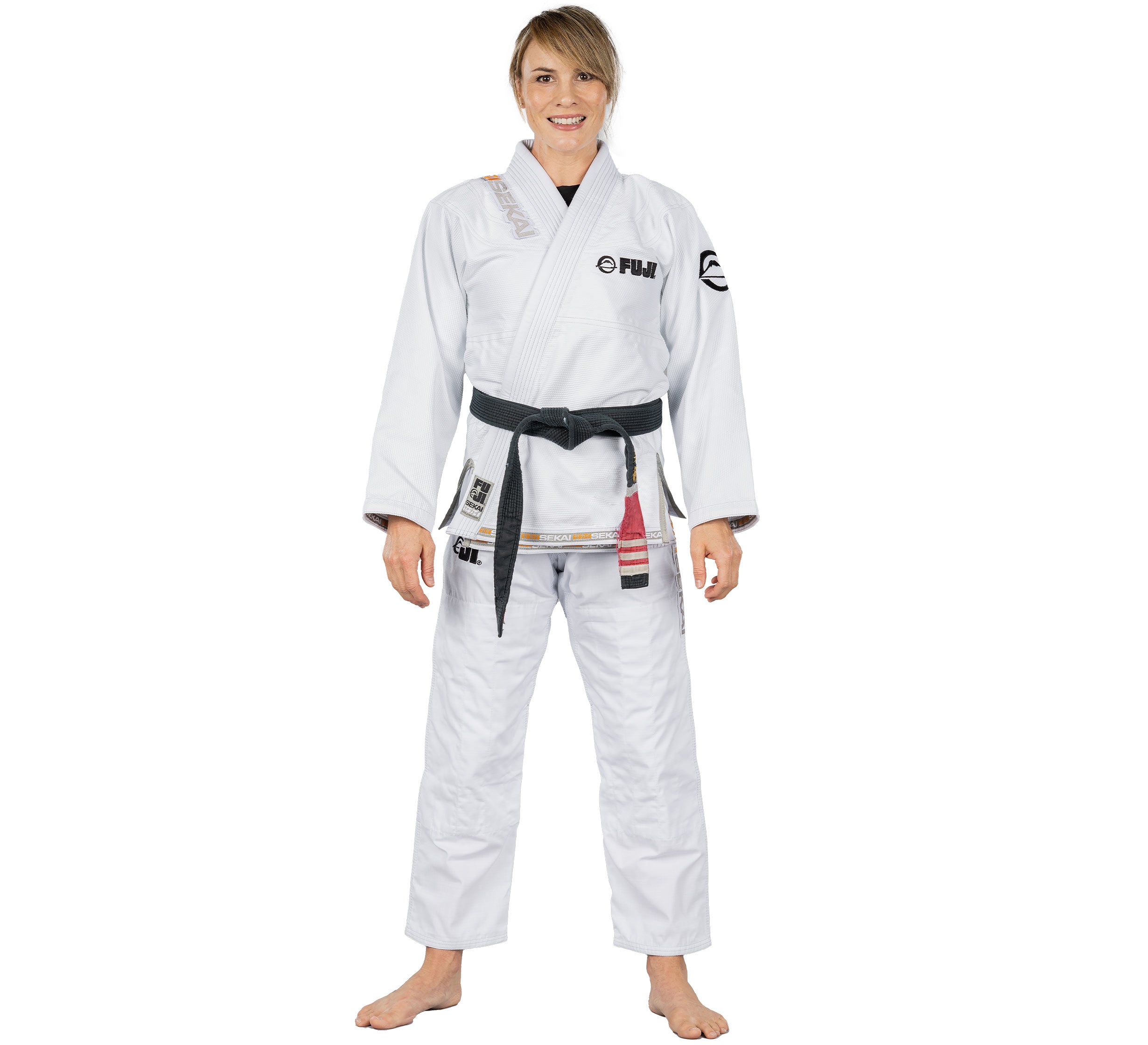 A woman stands barefoot and smiling, facing forward against a plain white background, wearing the Sekai 2.0 Womens BJJ Gi White with a black belt.