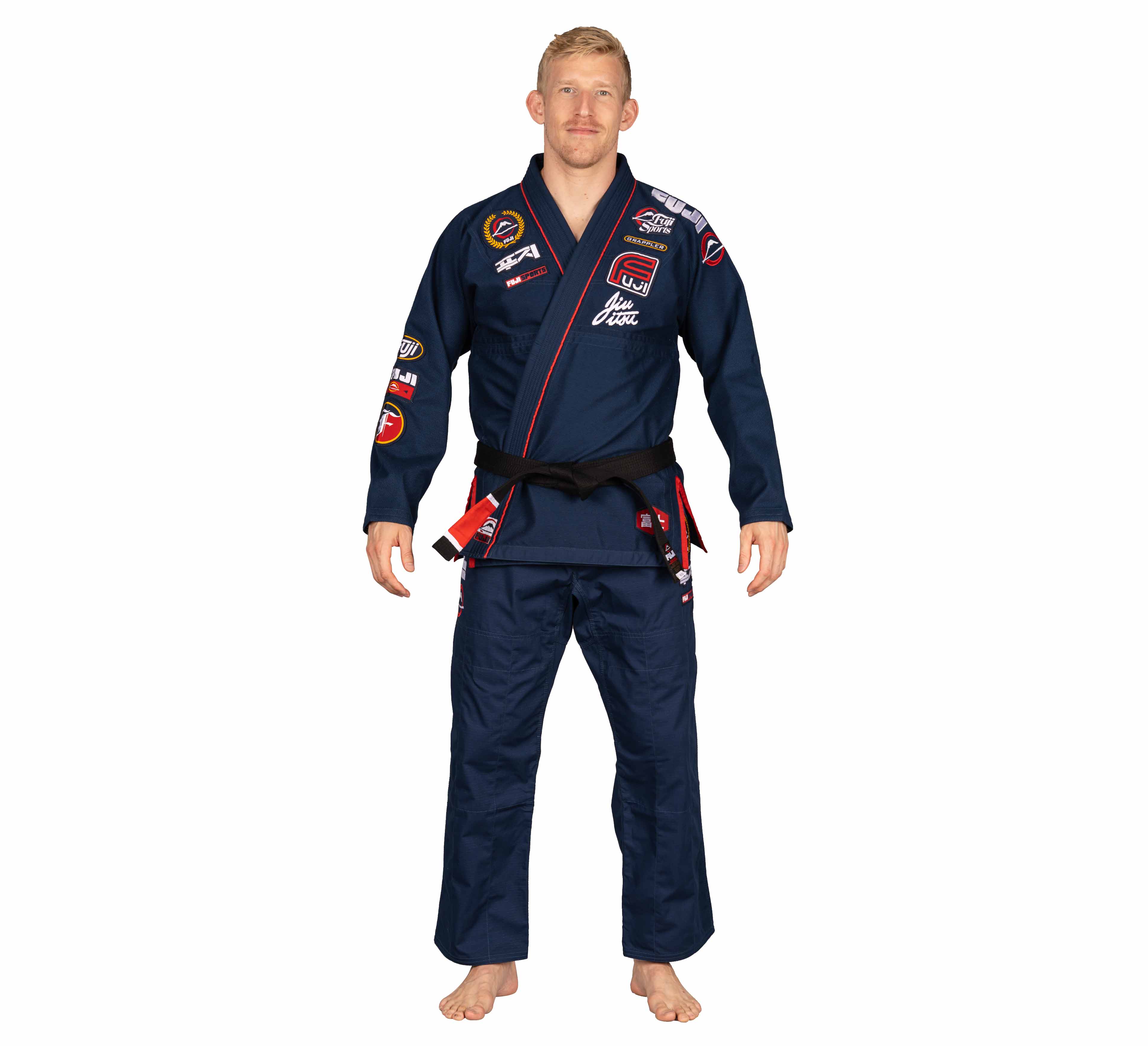 A man with short blond hair stands barefoot on a white background, facing forward with arms relaxed at his sides, wearing the Suparaito BJJ Gi XTR Edition Navy with patches and a black belt.