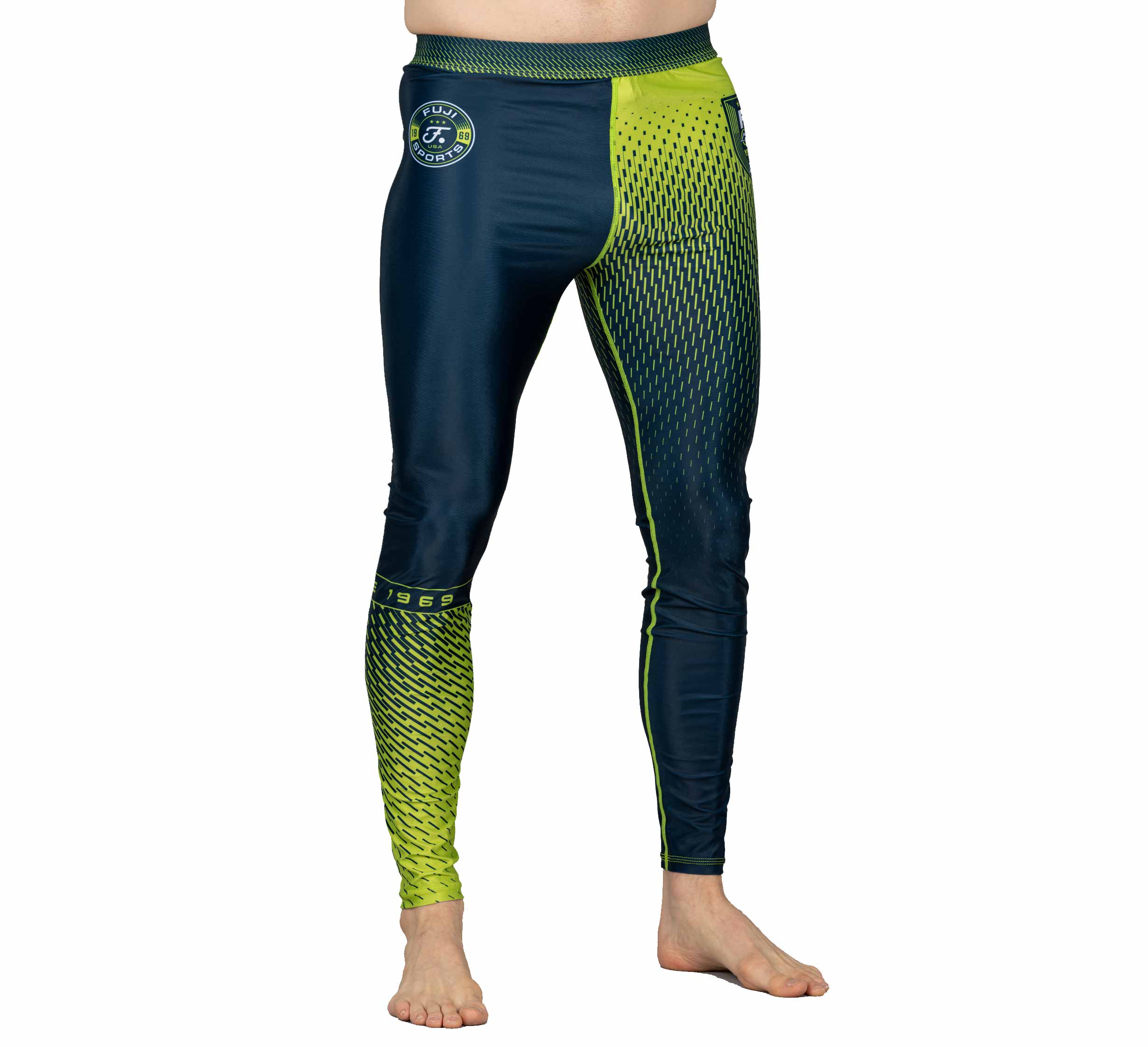 A person stands barefoot against a white background wearing Match Grappling Spats Navy—compression leggings with blue and neon green geometric patterns and a small logo on the left hip.