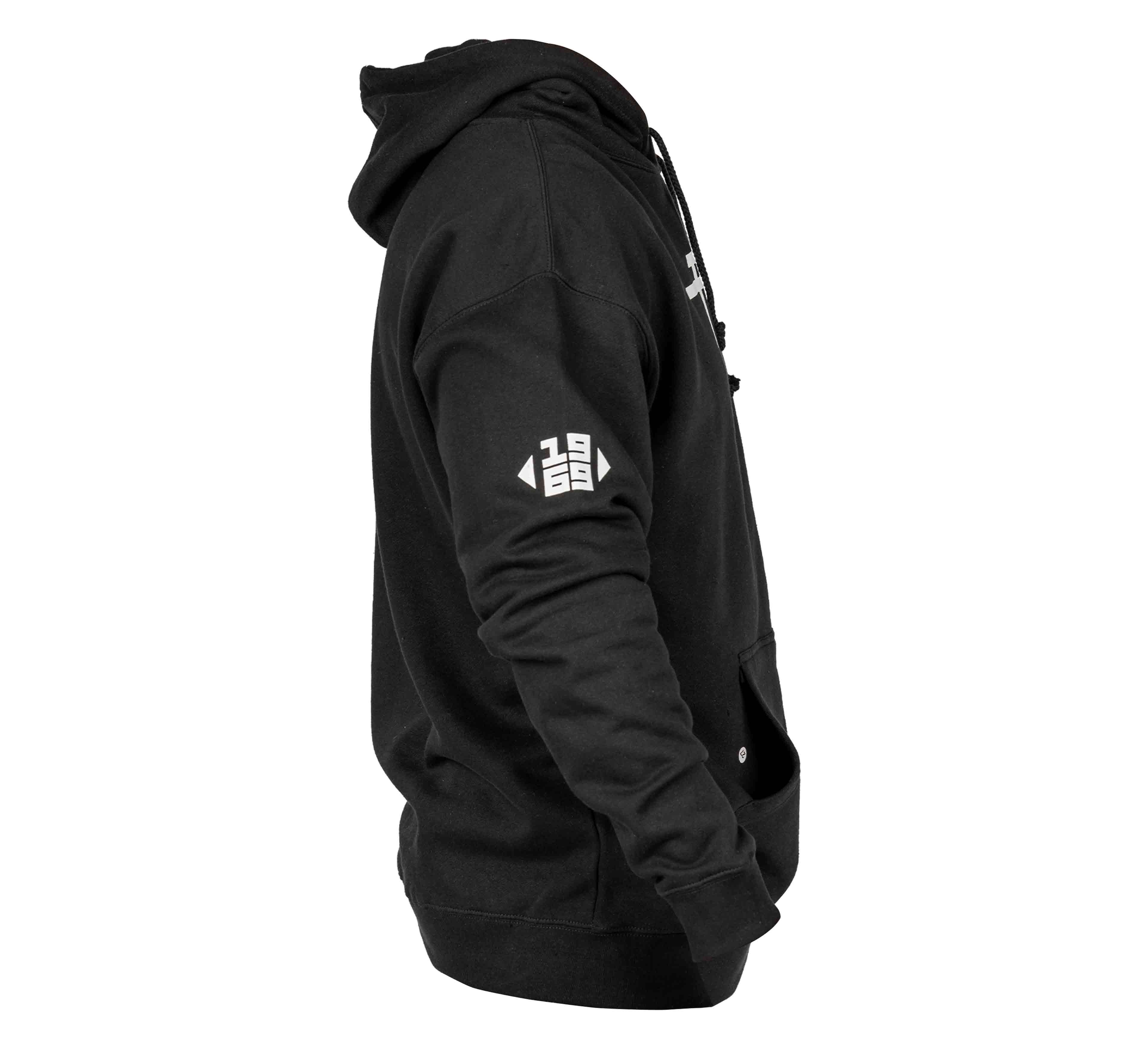 The Midnight Collegiate Pull Over Hoodie in black is shown from the side, with a white geometric logo on the upper sleeve, front pocket, and hood up. The partially visible front zipper adds detail. Unisex sizing available.