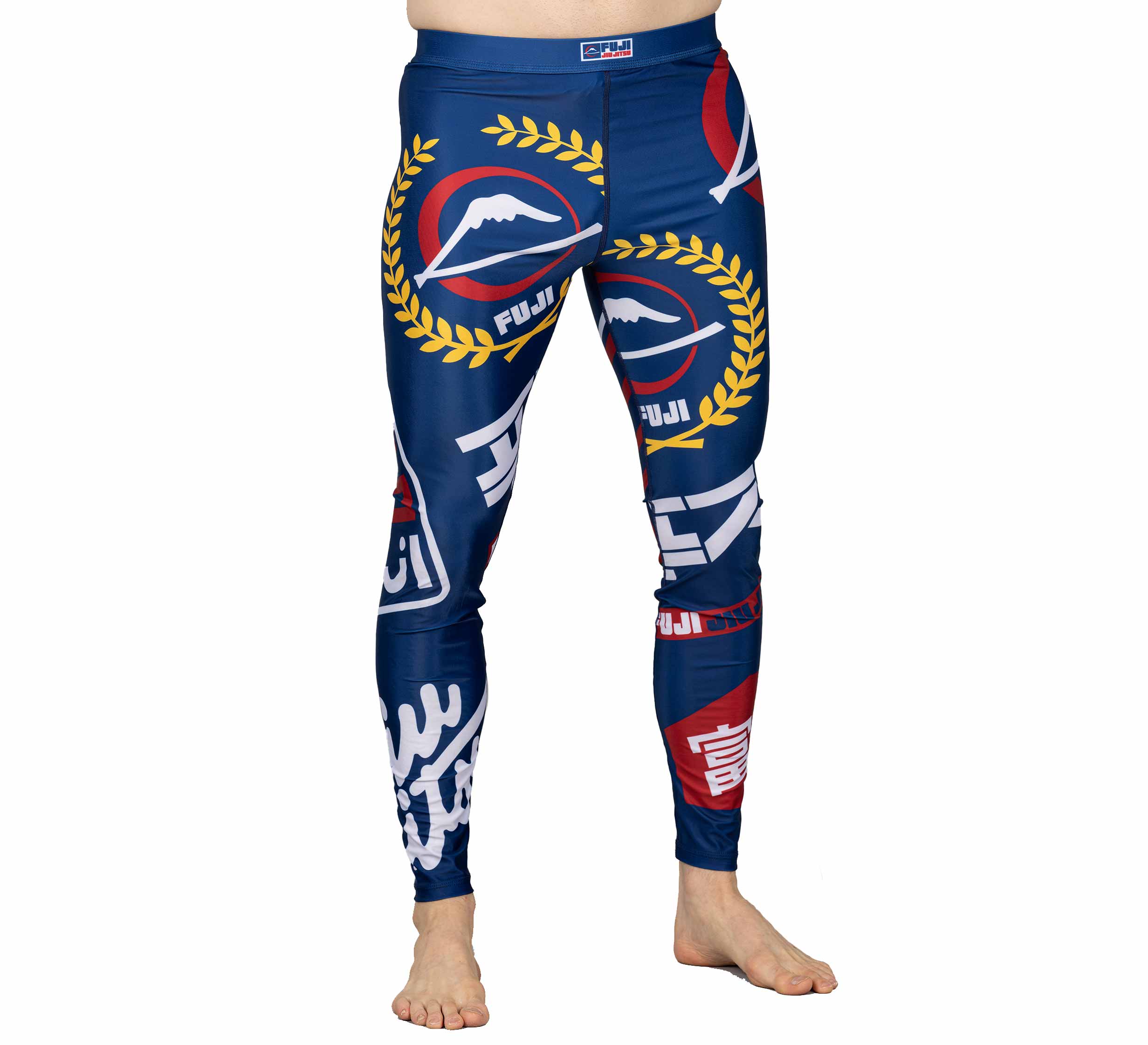 A person is wearing the XTR Extreme V1 Grappling Spats Navy, featuring Fuji logos, mountain graphics, and yellow laurel wreaths with red, white, and yellow printed designs. Only their lower body is visible and they are barefoot.