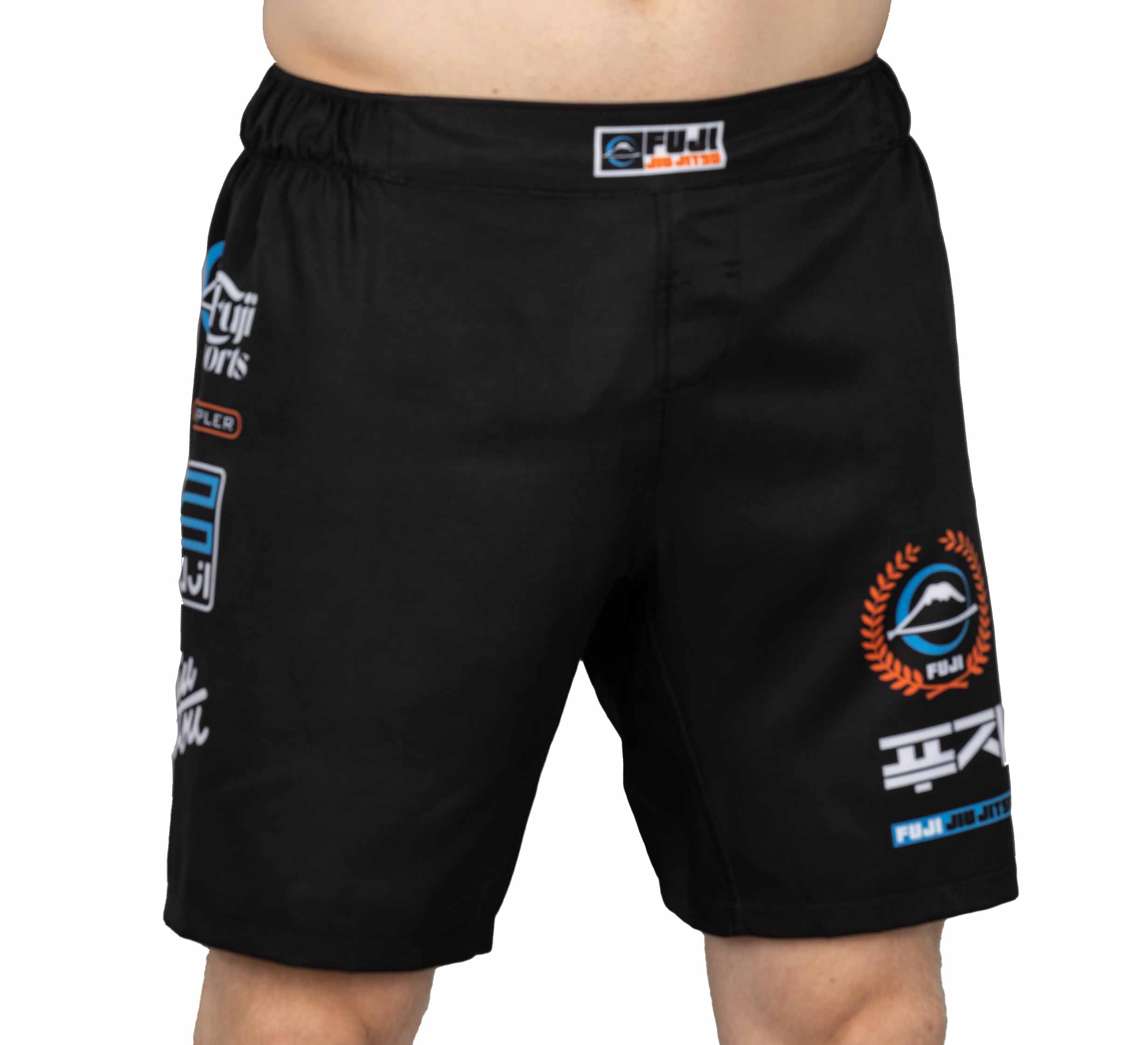 A person wearing XTR Extreme Grappling Fight Shorts Black, featuring an elastic waistband with a FUJI SPORTS label and white, blue, and orange logos/designs on the front. Only their lower torso and upper legs are visible.