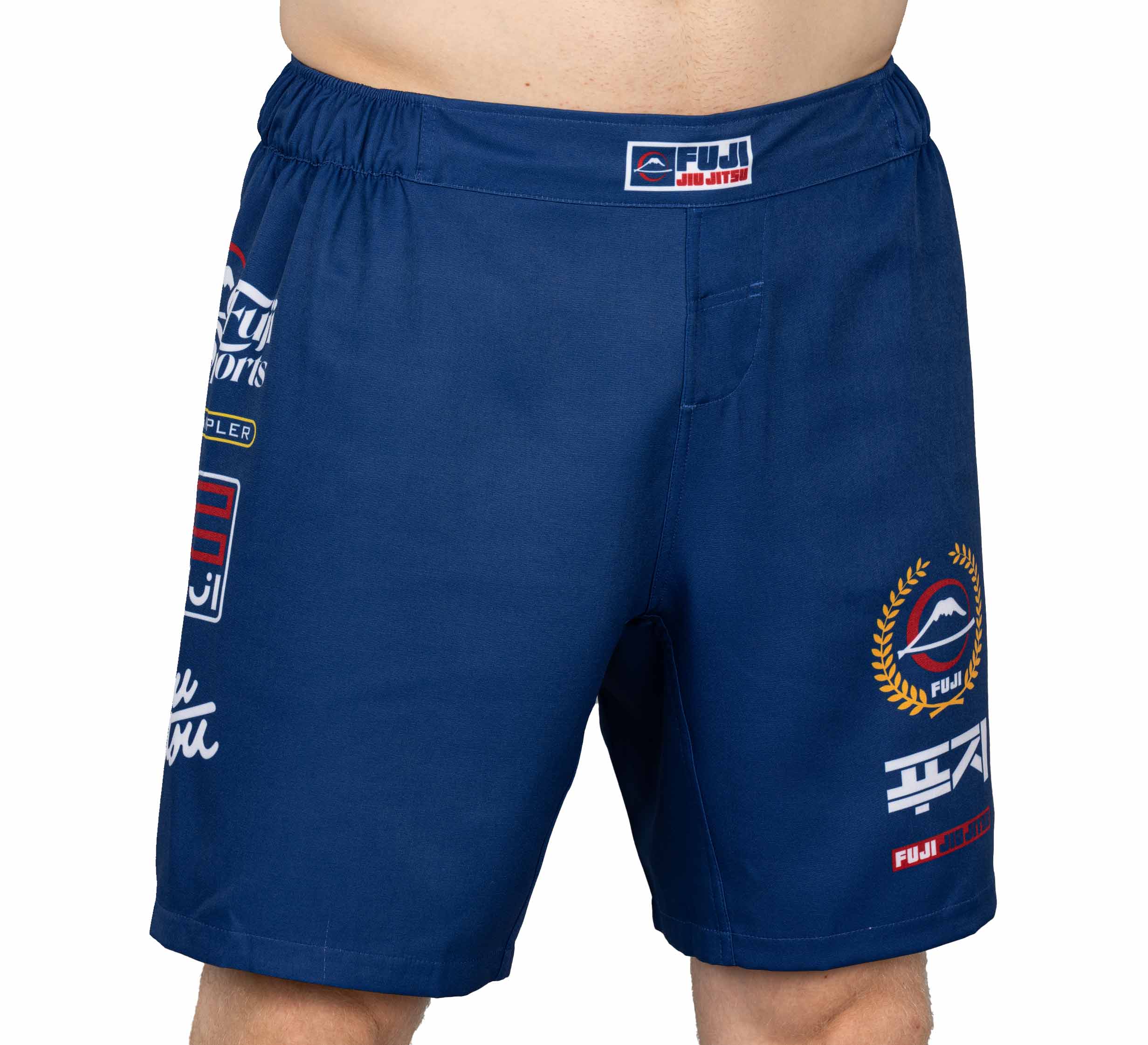 A person wearing XTR Extreme Grappling Fight Shorts Navy, featuring colorful patches and Fuji Jiu Jitsu logos, is shown from waist to mid-thigh against a plain white background.