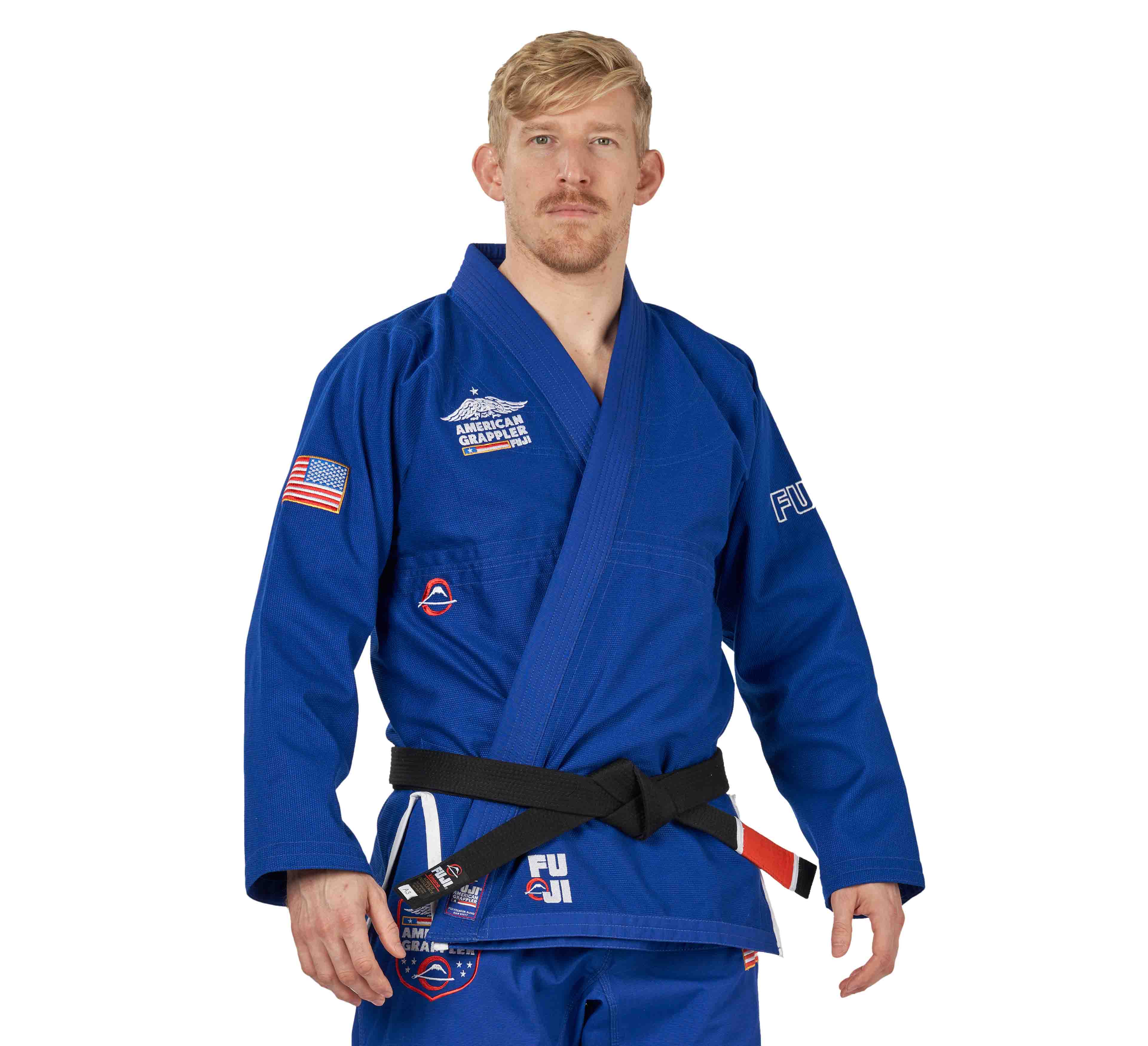 A man with short blond hair and a mustache wears the Suparaito BJJ Gi American Grappler Blue with patches and a black belt, standing and looking at the camera against a white background.