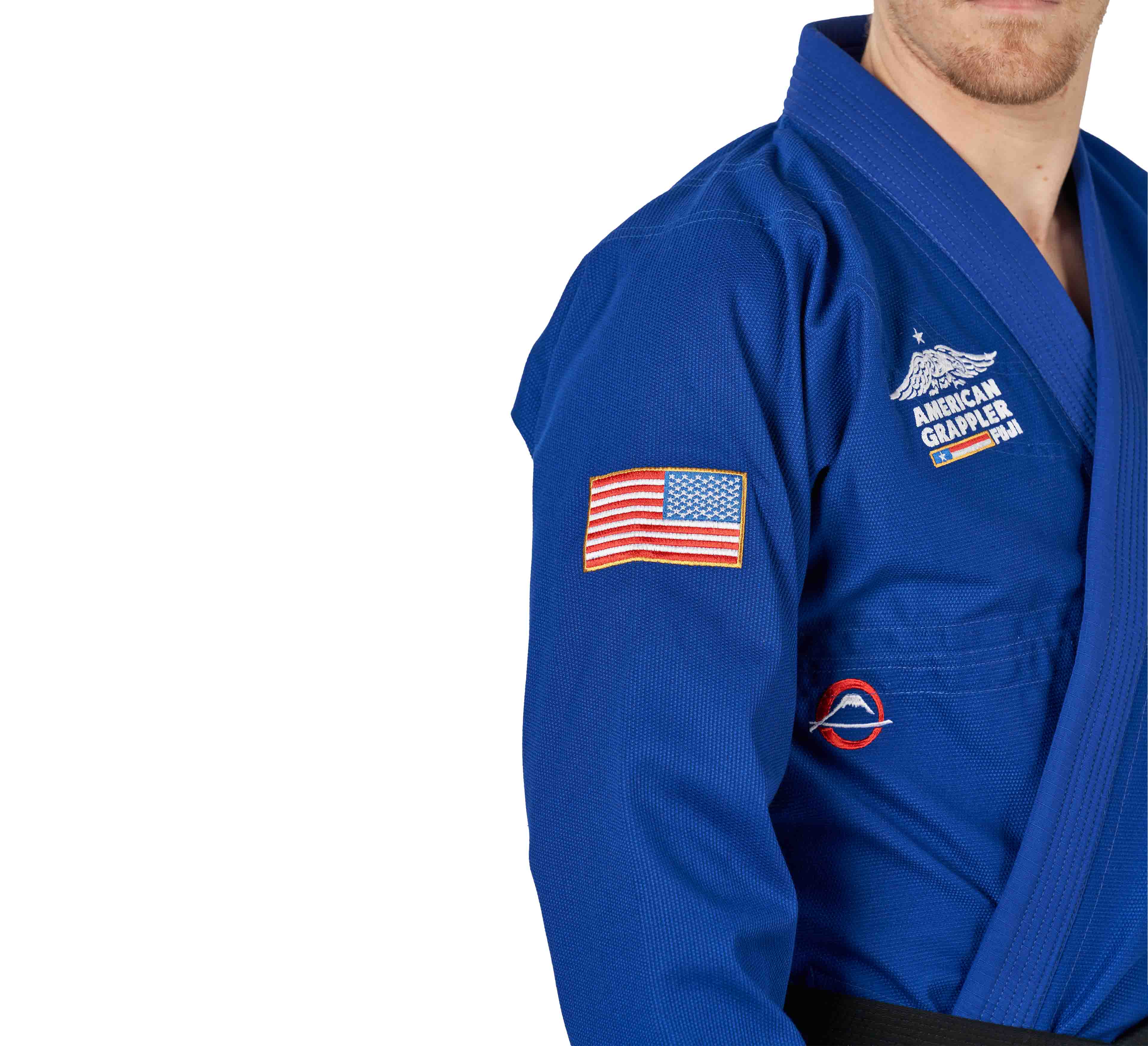 A person wears the Suparaito BJJ Gi American Grappler Blue, featuring an American flag patch on the sleeve and "American Grappler" text on the chest, partially visible from the chest up against a white background.