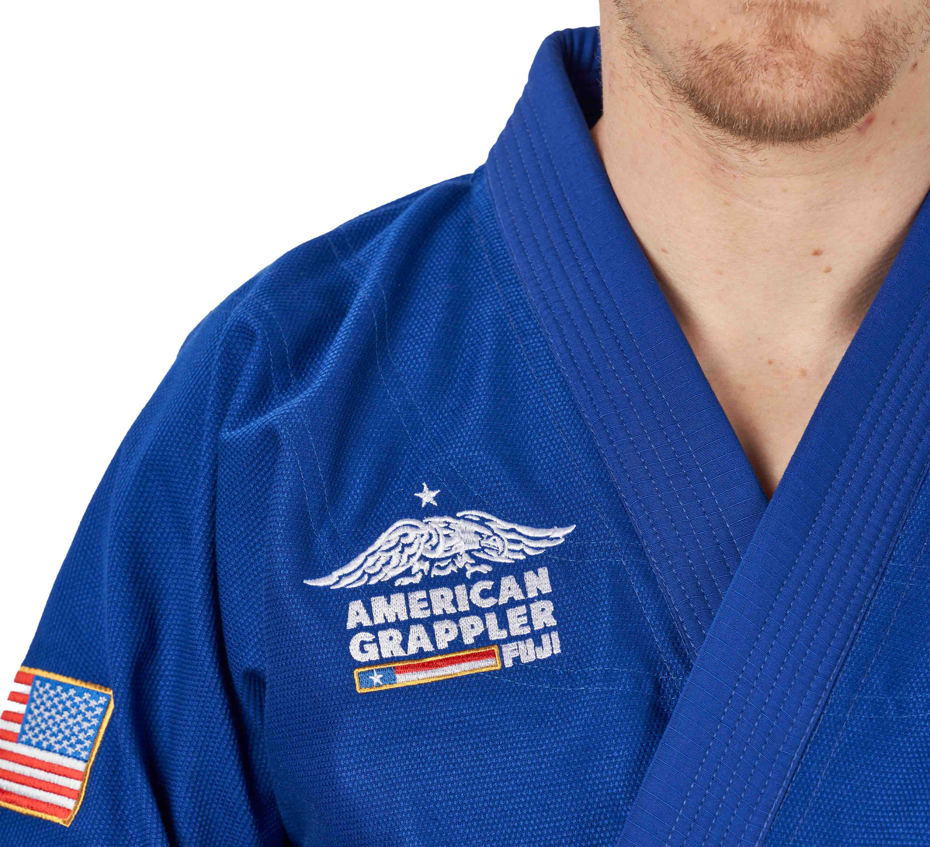 A person wearing the Suparaito BJJ Gi American Grappler Blue, featuring an embroidered eagle and "American Grappler Fiji," plus an American flag patch on the sleeve.