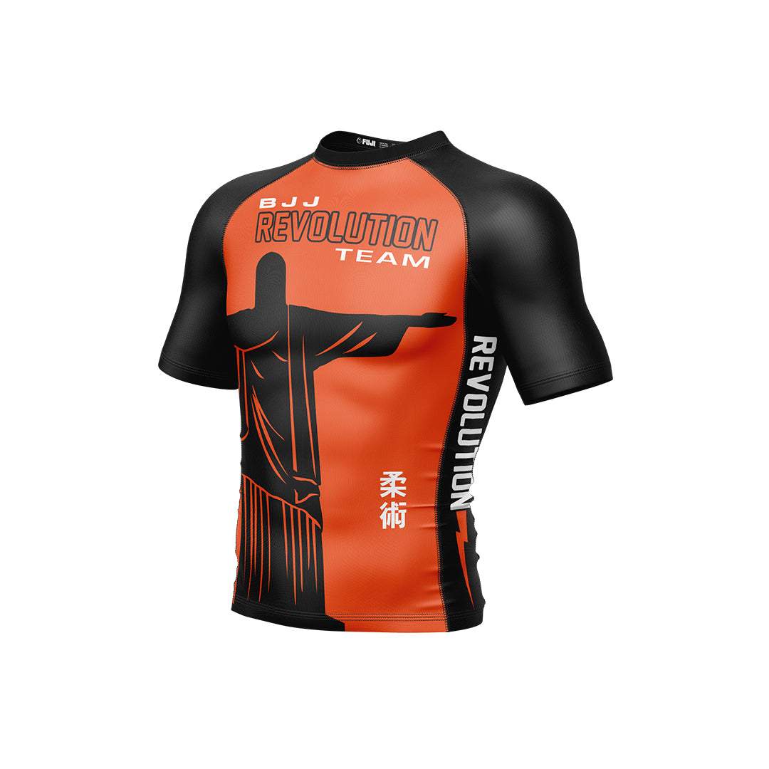 The BJJ Revolution KIDS Ranked Rashguard Short Sleeve in orange features “BJJ Revolution Team” text, a Christ the Redeemer image, white Japanese characters, and “REVOLUTION” printed vertically on the left.