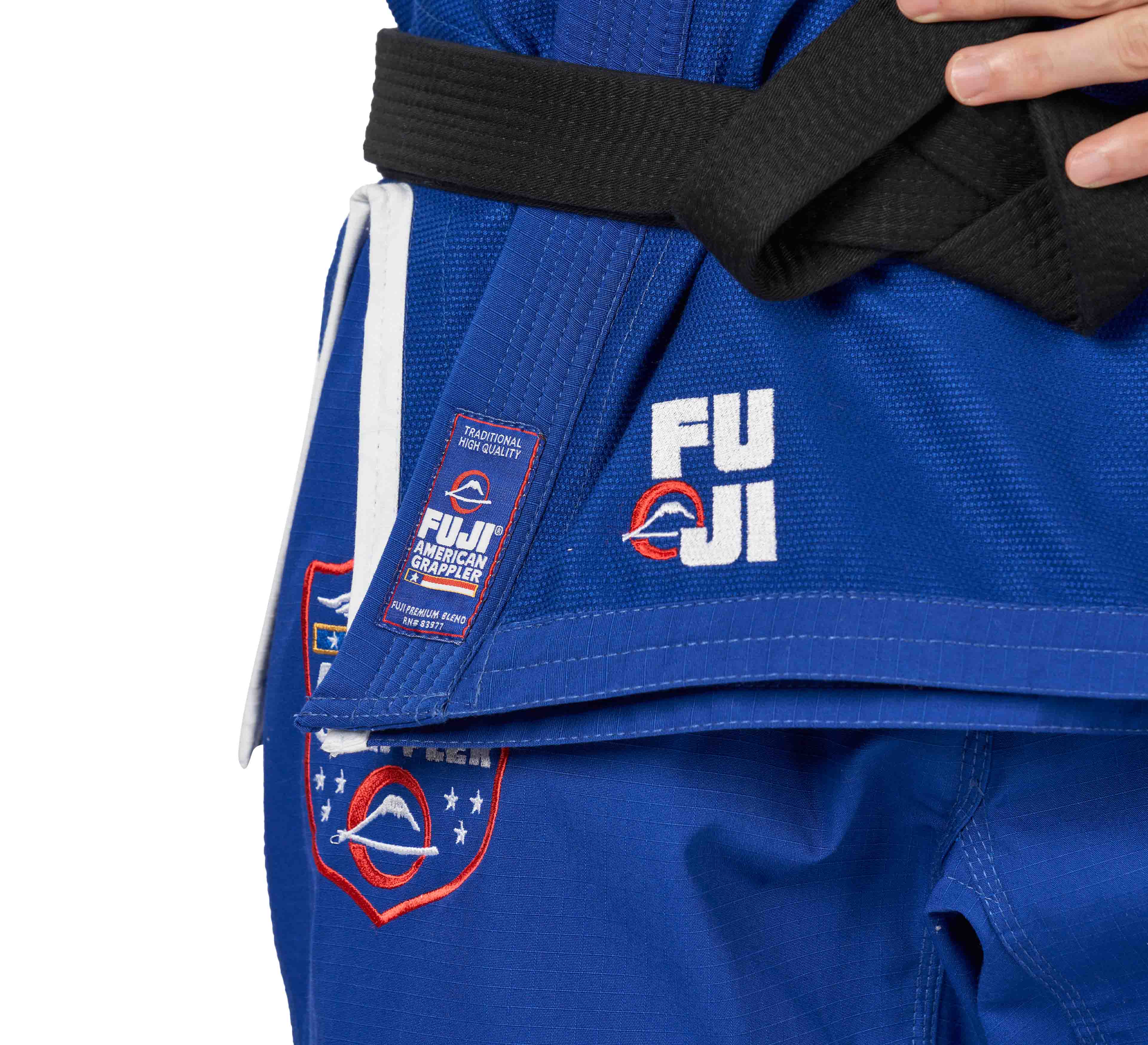 A person wearing the Suparaito BJJ Gi American Grappler Blue with FUJI and American Grappler patches and a black belt; only their torso and hip area are shown.