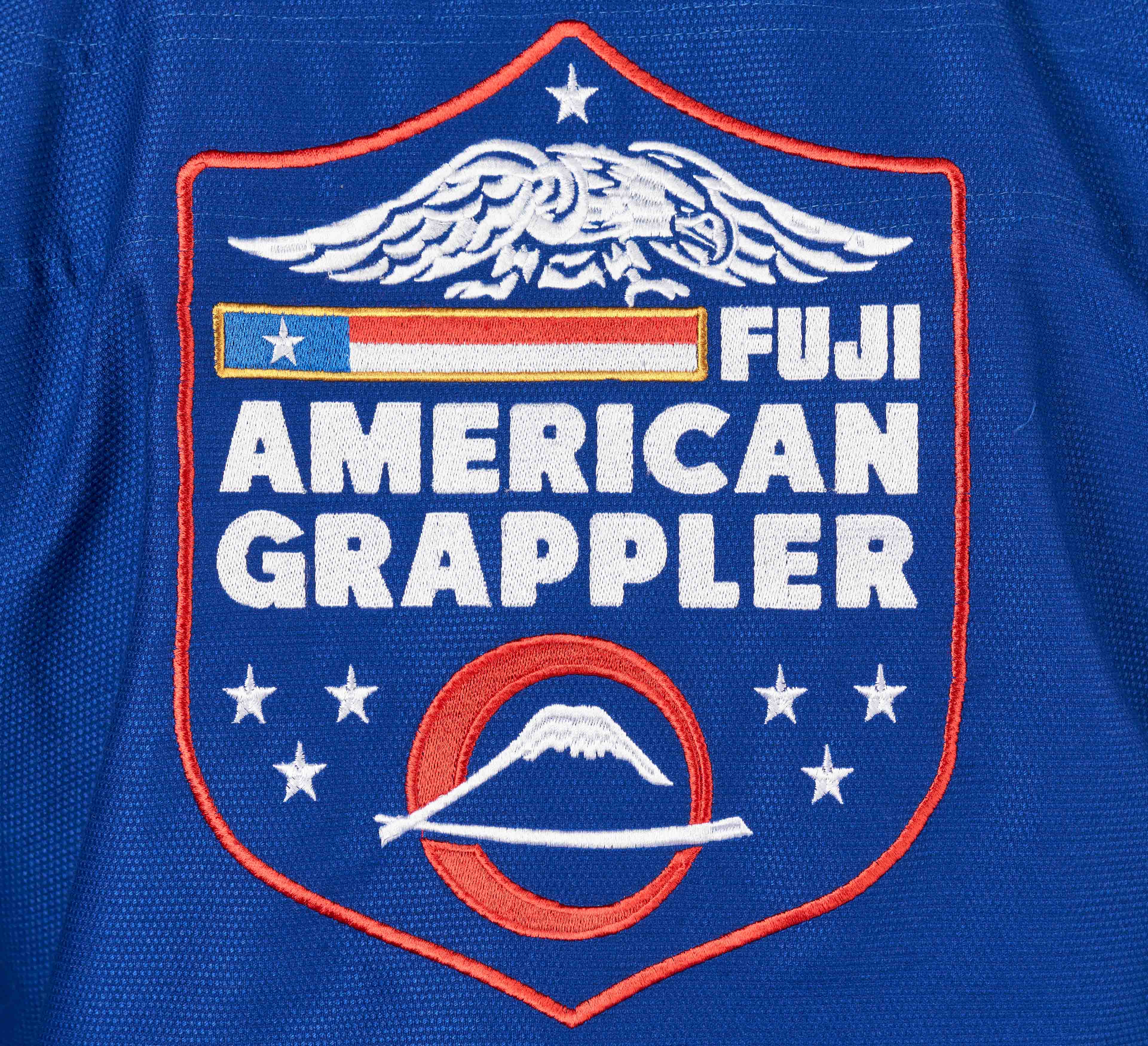 The Suparaito BJJ Gi American Grappler Blue features a blue patch with a bald eagle, stars, “FUJI American Grappler” text, plus a stylized American flag and Mount Fuji in the design.