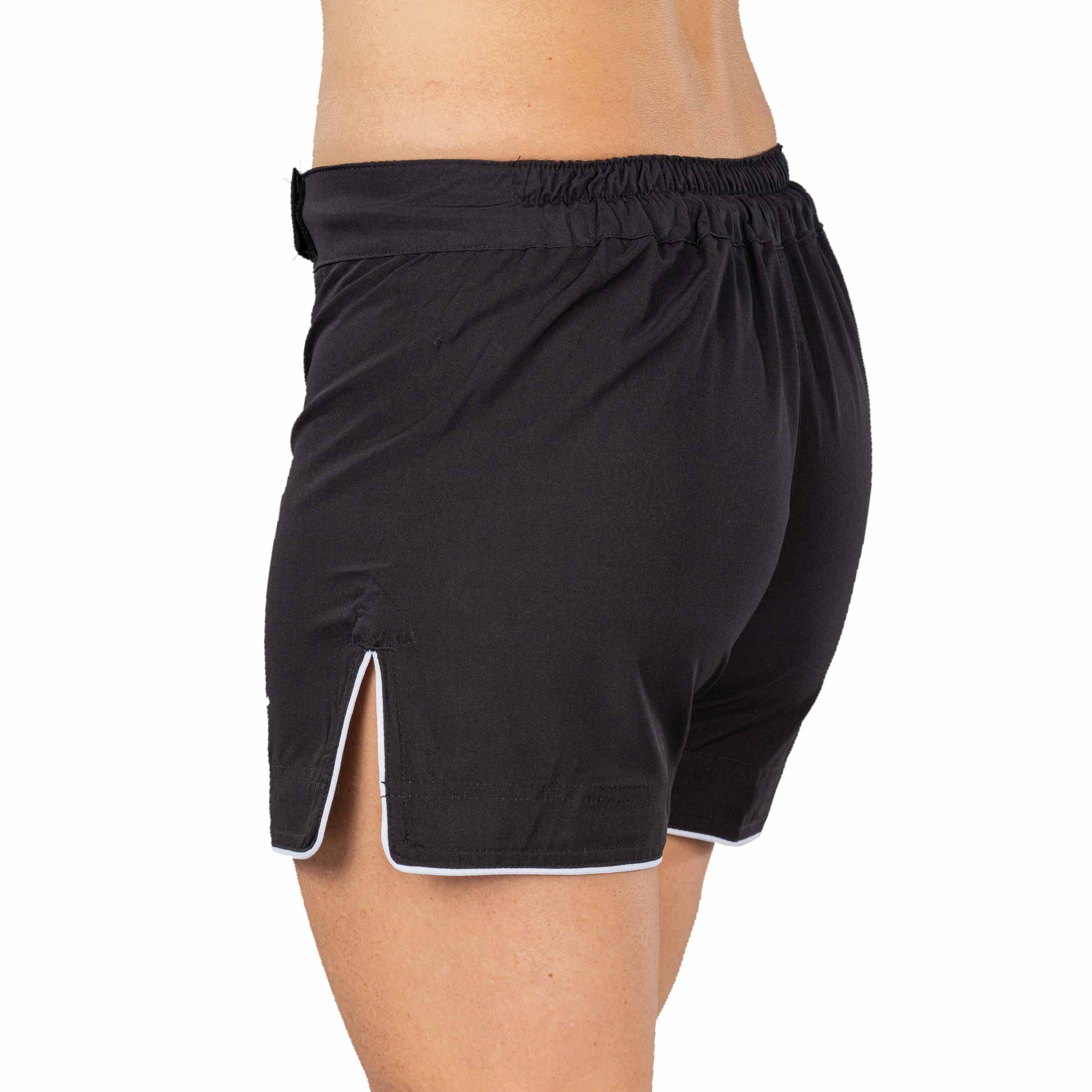 A woman is seen from the side and slightly behind wearing Baseline Womens Black Grappling Shorts, featuring white trim, an elastic waistband, and side slits.