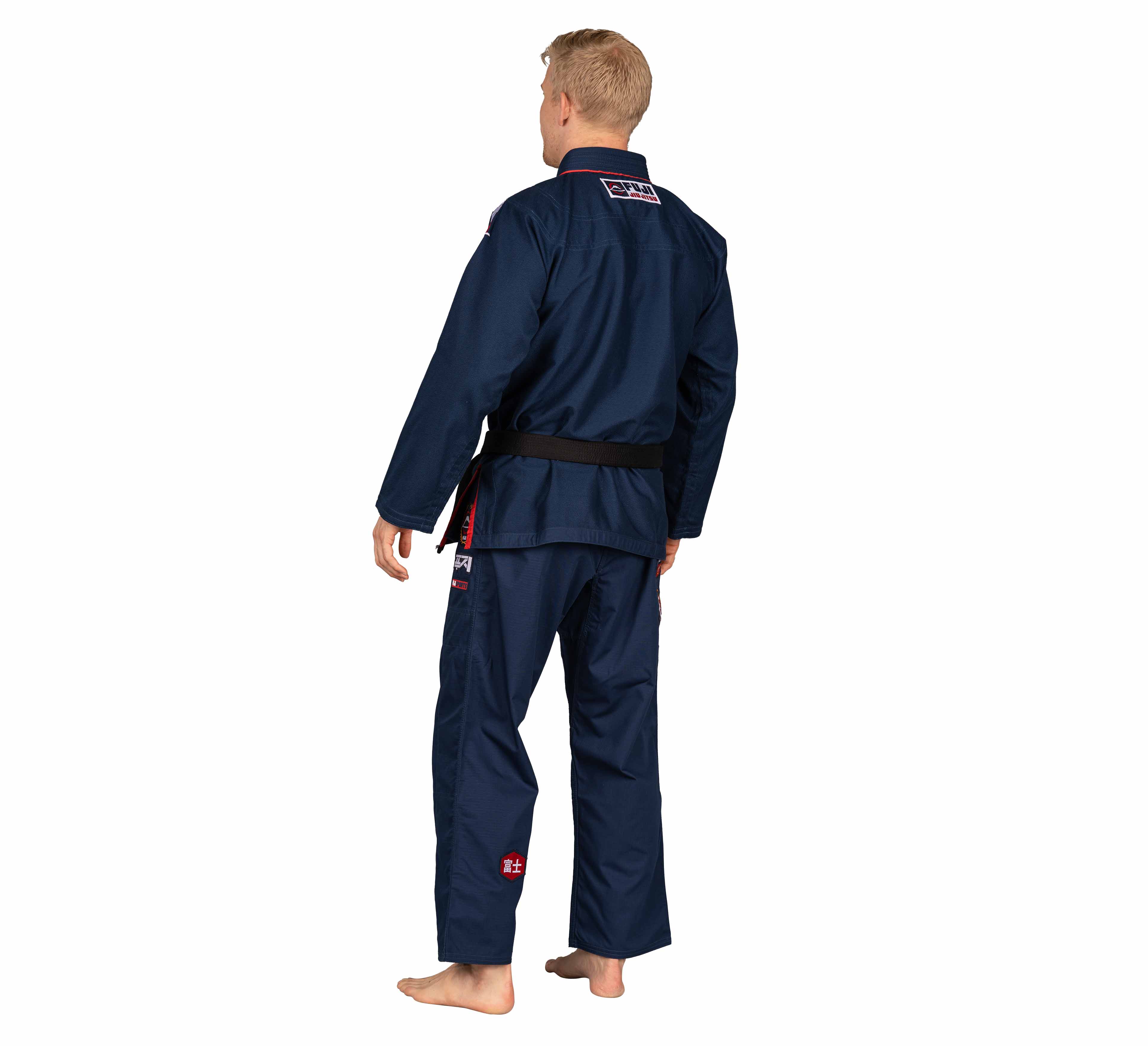 A barefoot person stands facing away in a Suparaito BJJ Gi XTR Edition Navy with a black belt and patches, set against a plain white background.