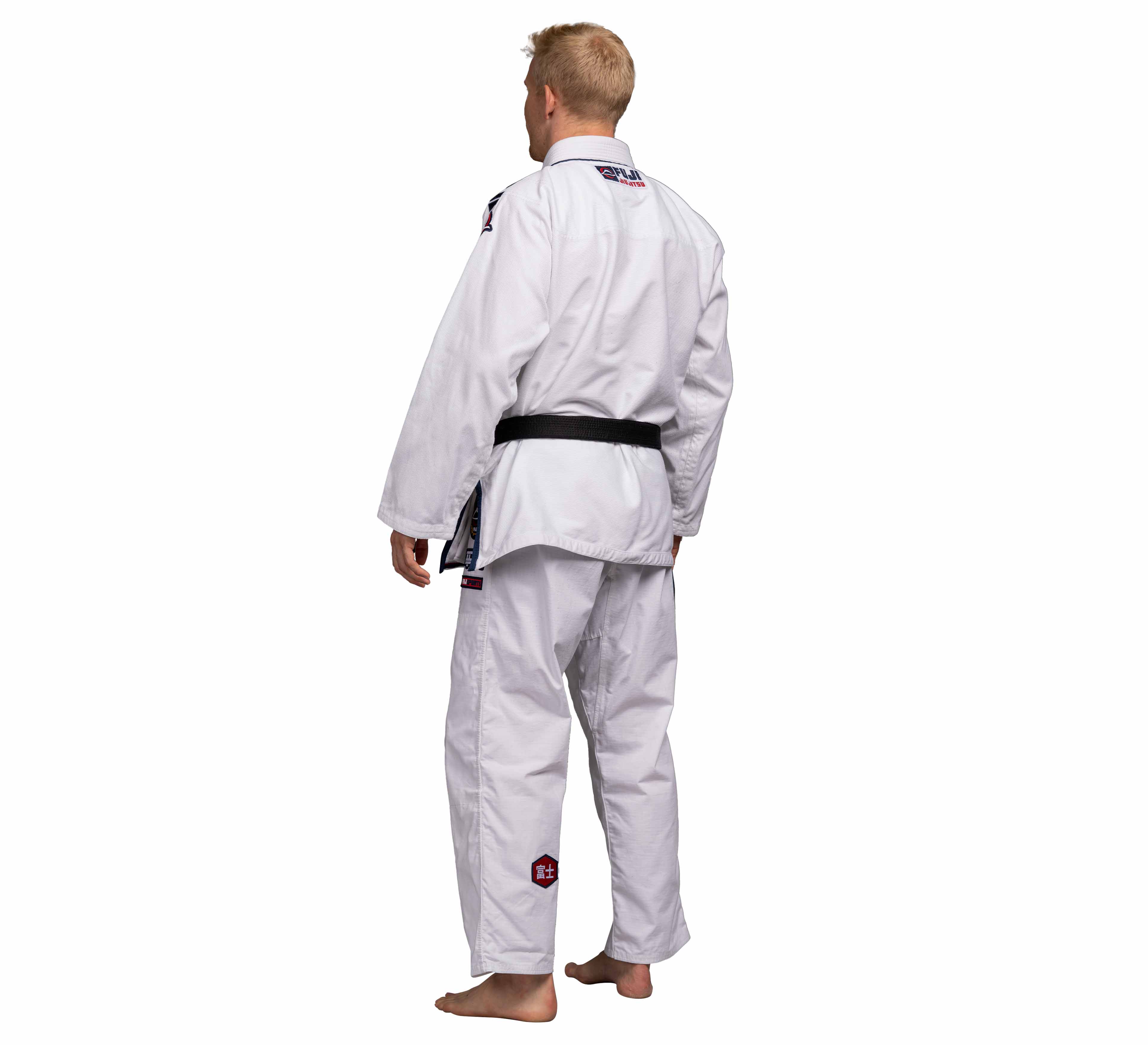 A person stands barefoot, facing away from the camera in a Suparaito BJJ Gi XTR Edition White with a black belt, against a white background.