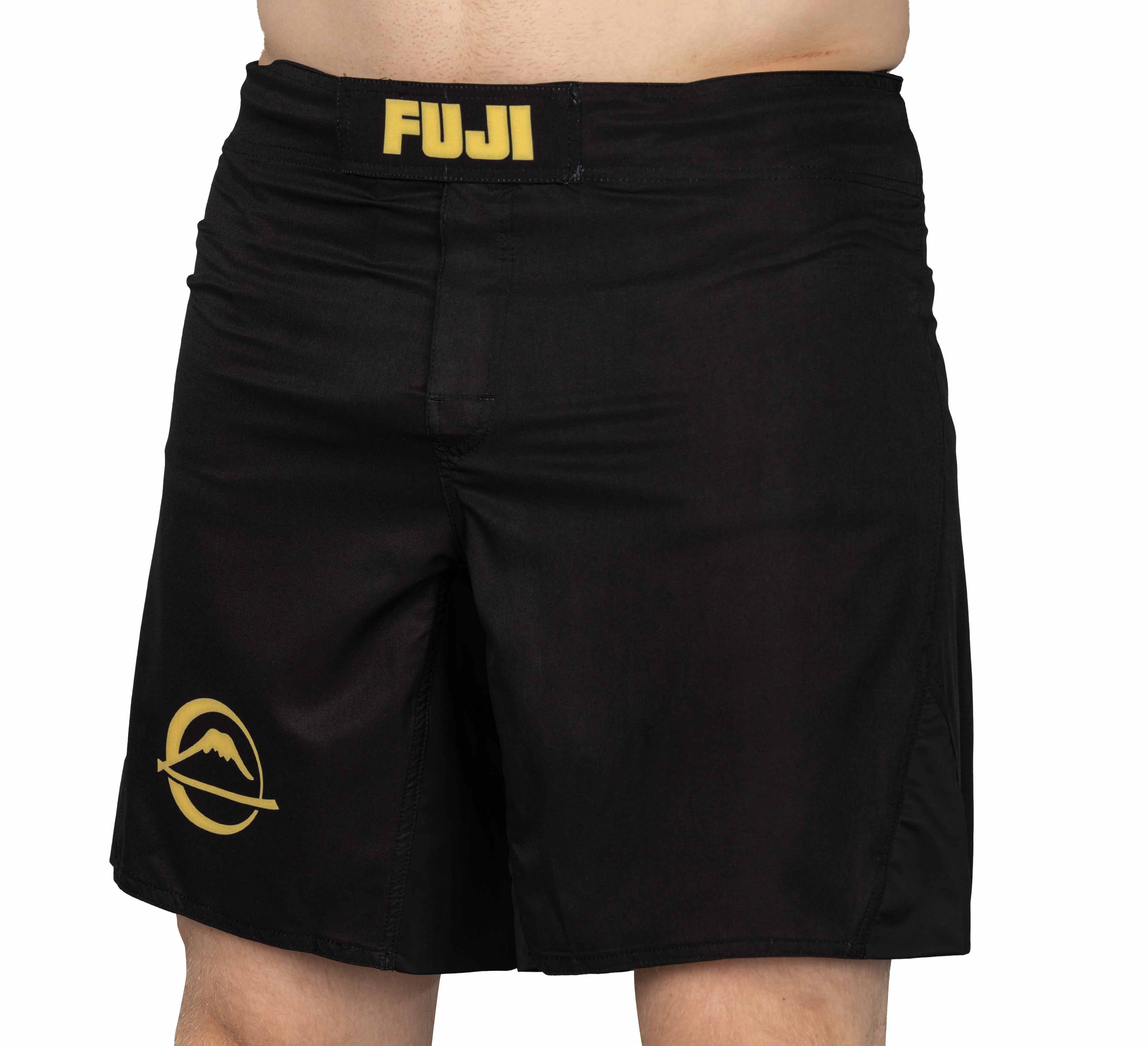 A person wearing Baseline Fight Shorts Black/Yellow with "FUJI" in gold on the waistband and a gold mountain logo on the left leg. The person's torso and legs are partially visible.