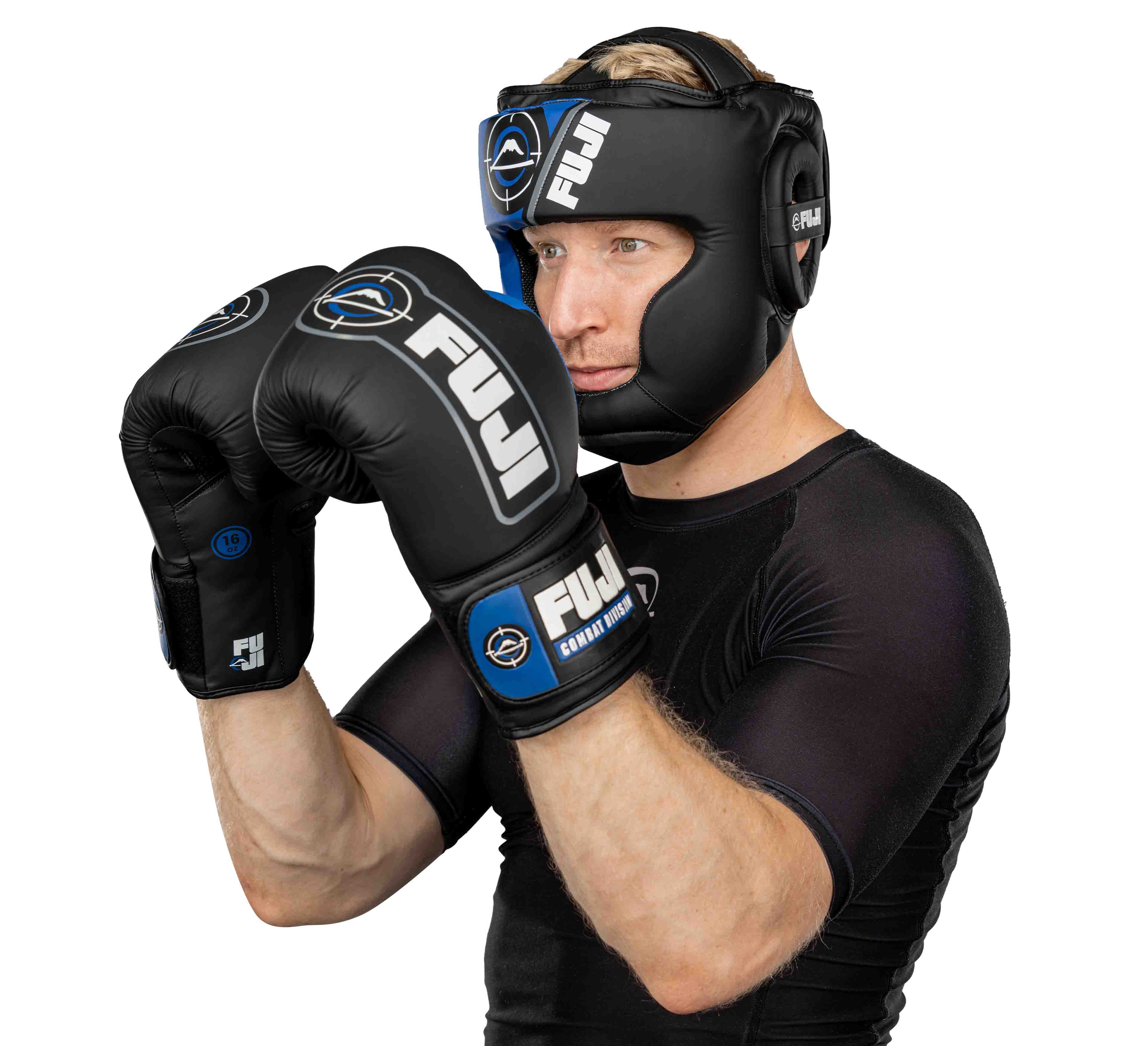 A man wearing black FUJI boxing gloves and Precision Striking Headgear stands in a defensive boxing stance against a white background.