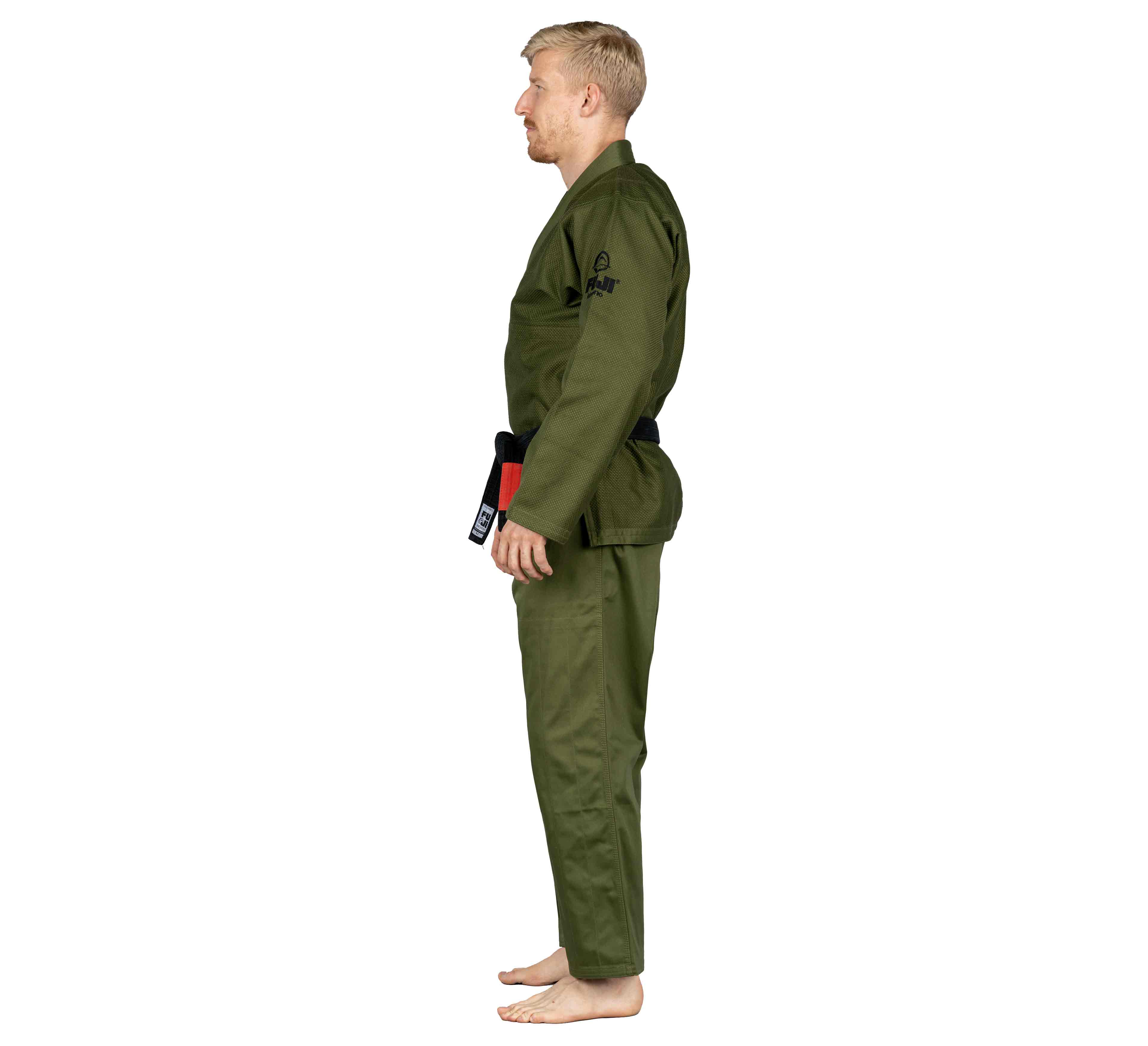 A man with short blond hair, dressed in the All Around BJJ Gi Military Green and a black belt, stands barefoot in side profile against a plain white background.