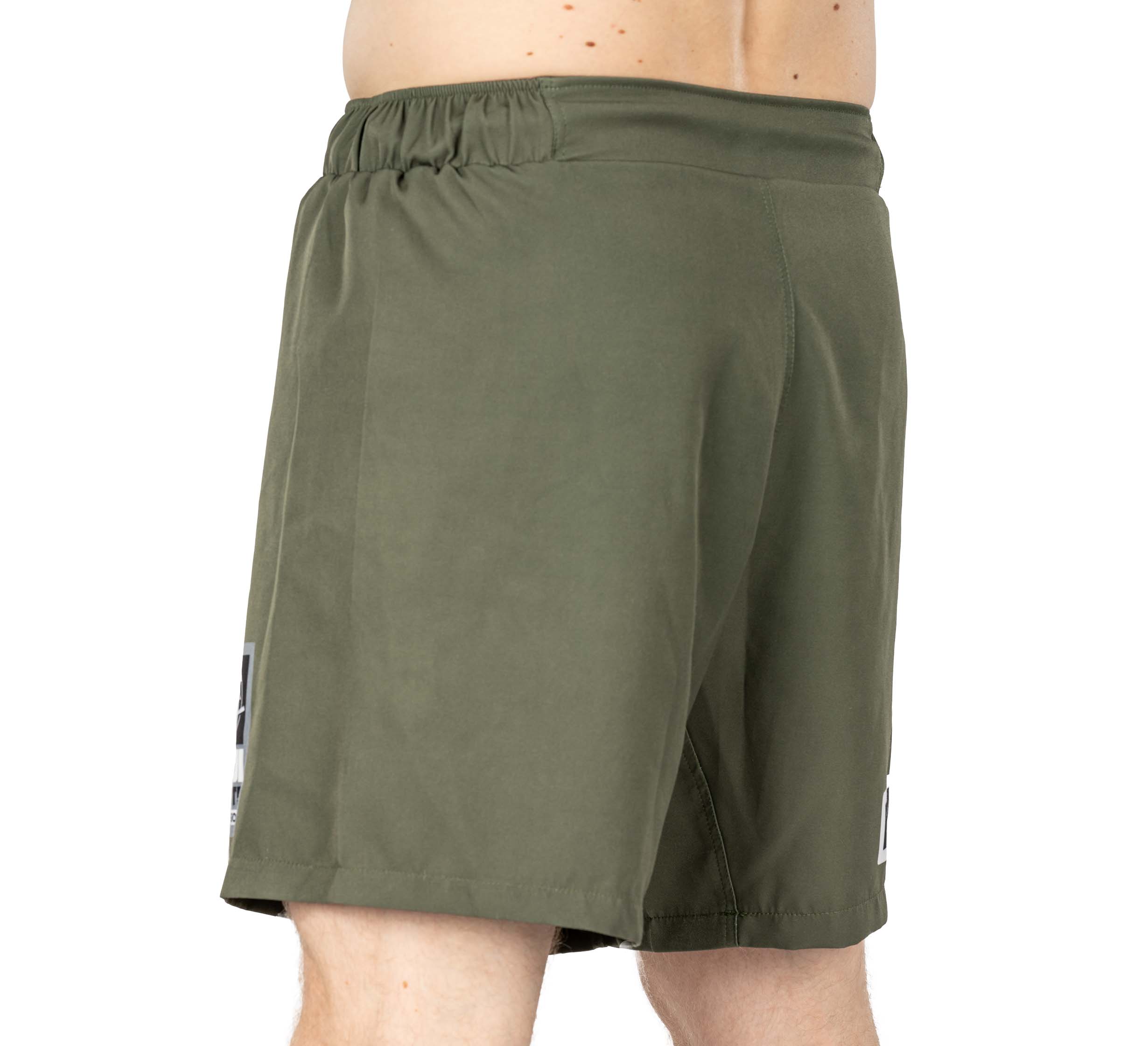 A person wearing Ultimate Grappling Shorts in military green with an elastic waistband, viewed from the side against a white background. Only the lower torso and upper legs are visible.