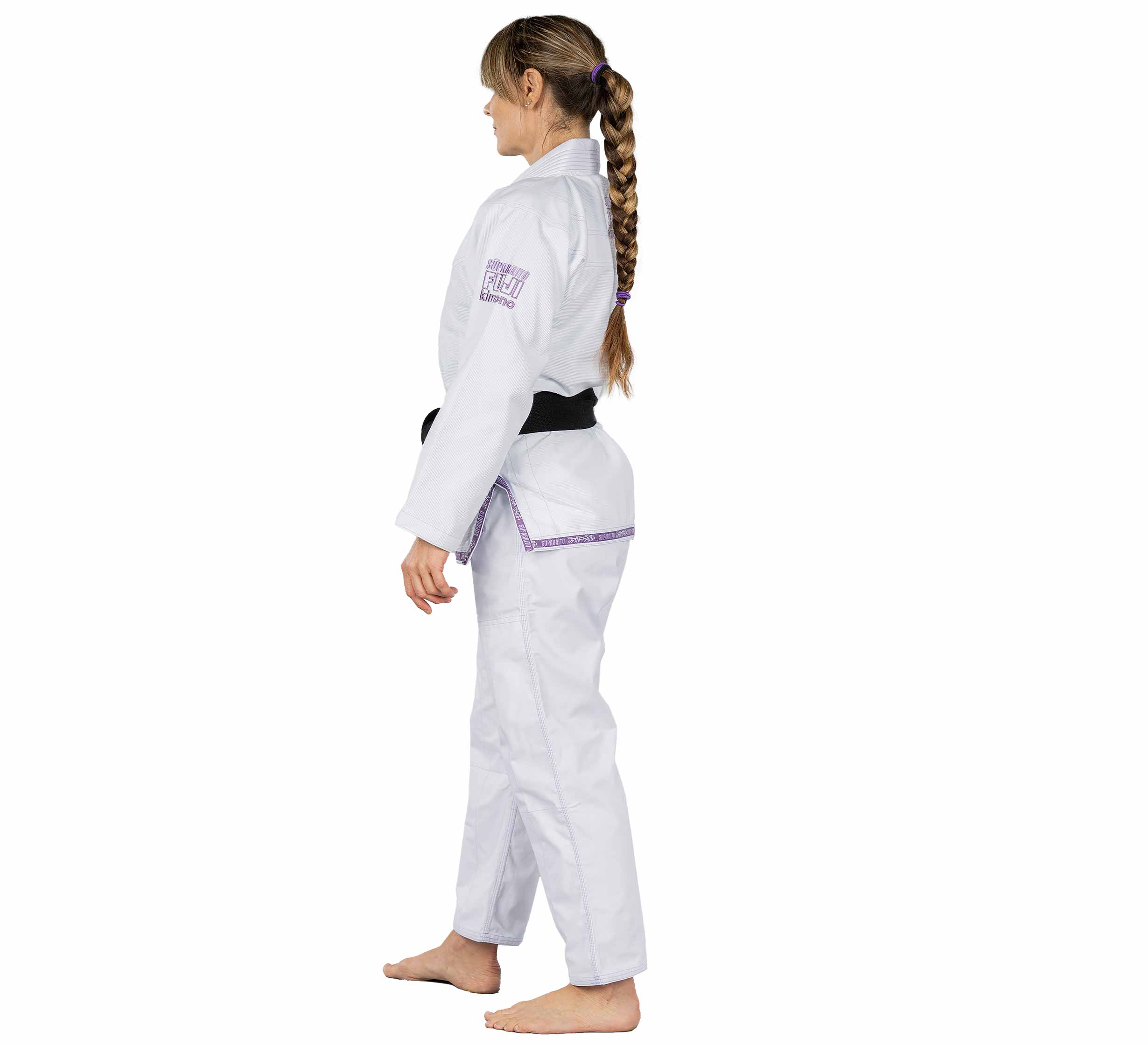 A woman with a long braid stands barefoot, facing sideways in the Suparaito Womens BJJ Gi Purple and black belt against a plain white background.