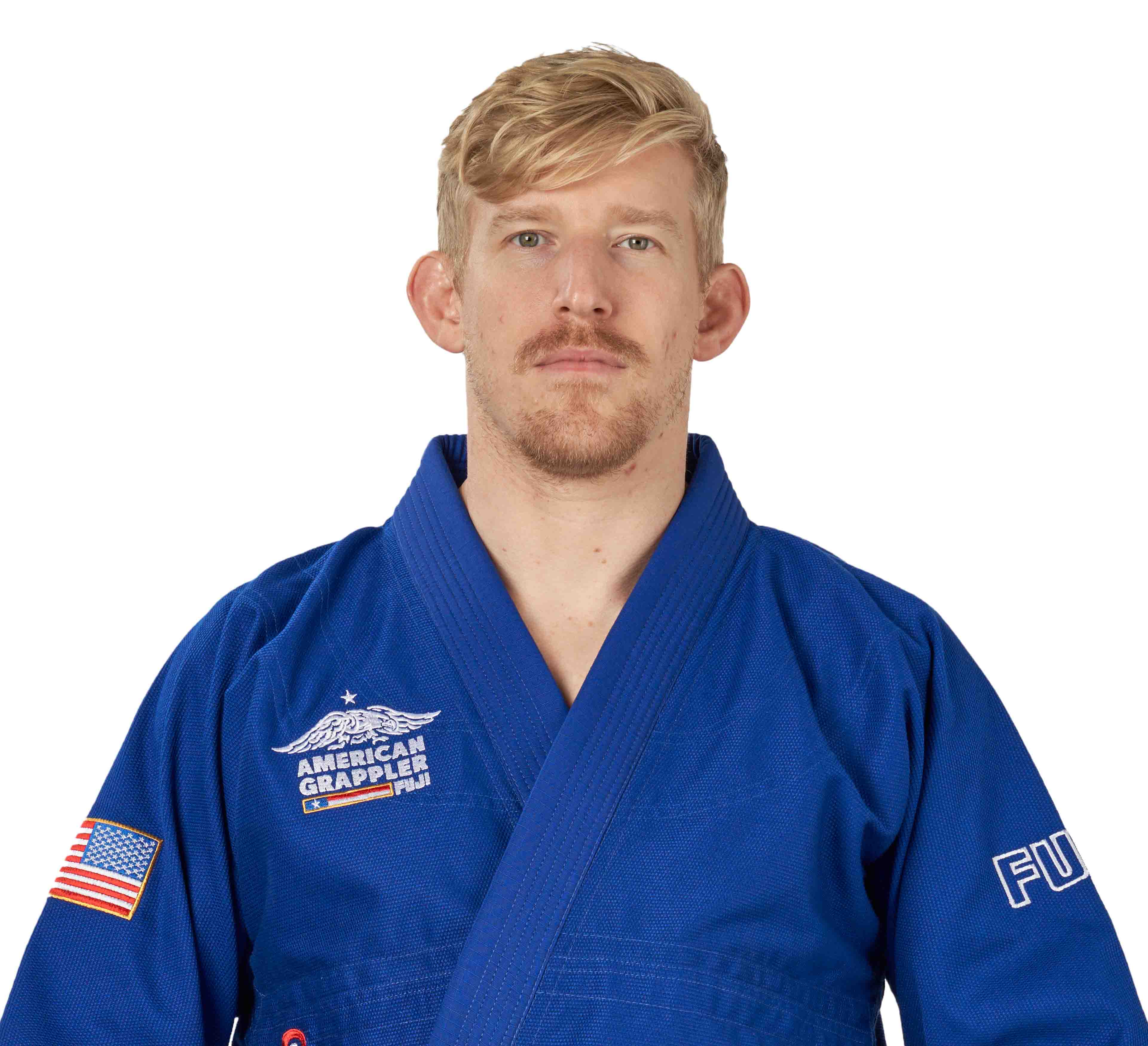 A blond man with a mustache wears the Suparaito BJJ Gi American Grappler Blue, featuring patches like an American flag and “American Grappler.” He stands against a white background, facing the camera.