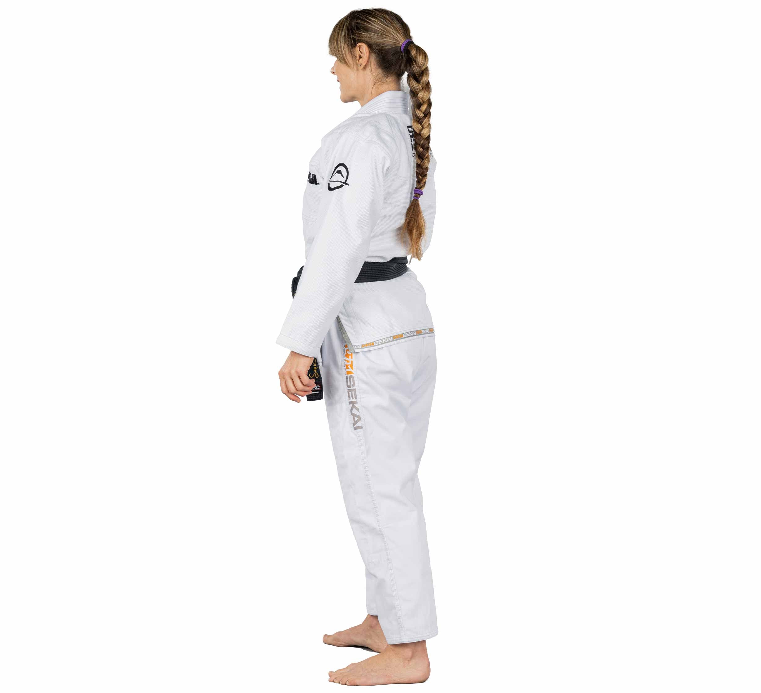 A woman wearing the Sekai 2.0 Womens BJJ Gi in white, barefoot and with a black belt, stands in profile facing left with her hair in a braid against a plain white background.