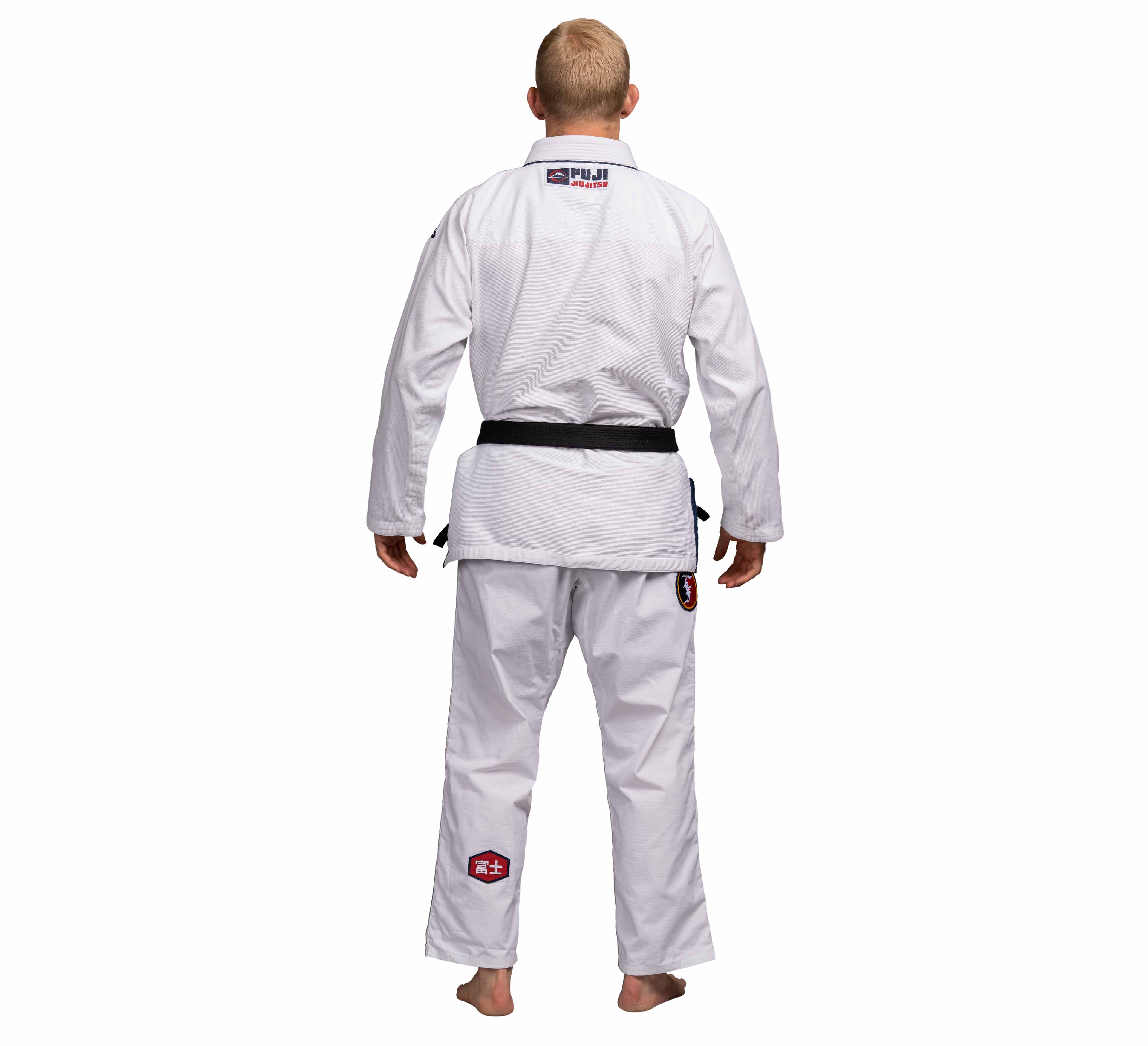 A person with short blond hair is standing barefoot, facing away, wearing a Suparaito BJJ Gi XTR Edition White with a black belt and patches on the back and pant leg.