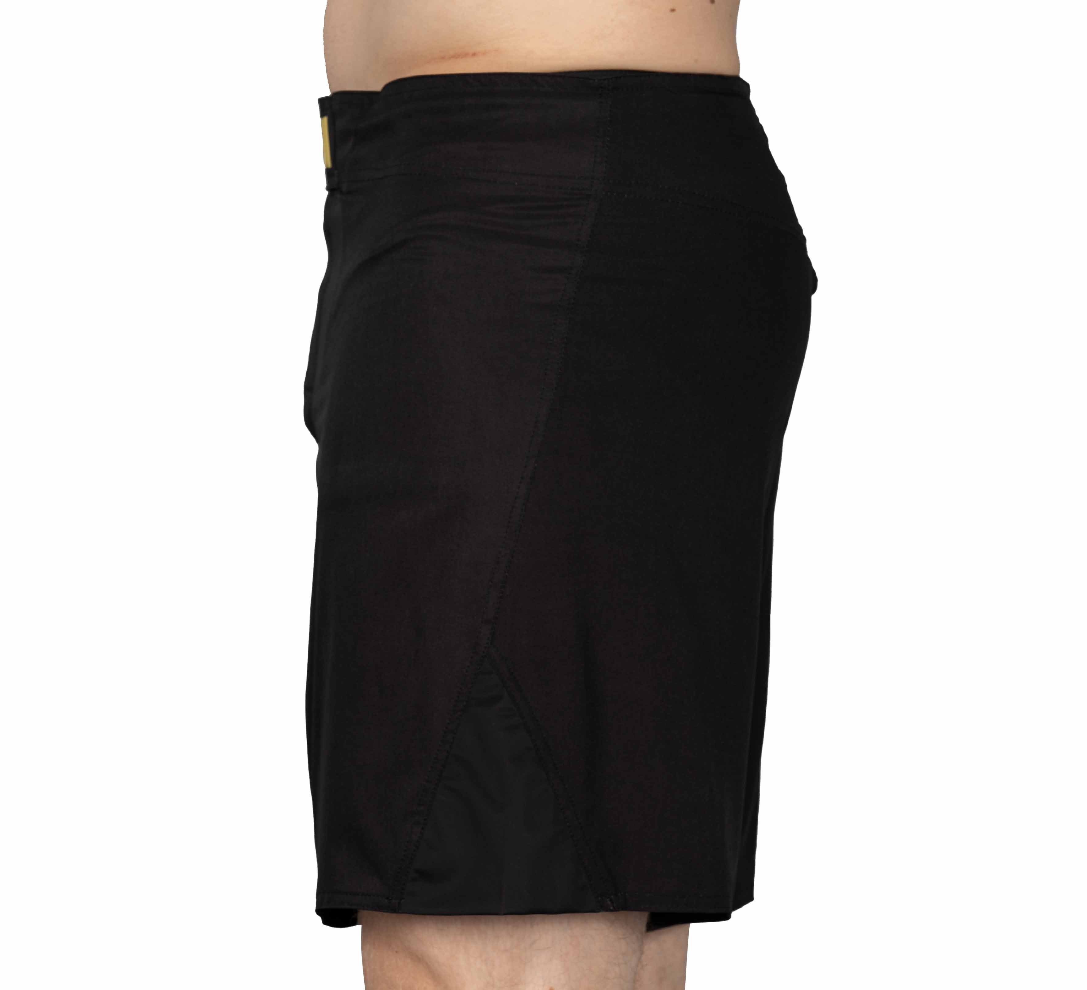 A person in profile displays Baseline Fight Shorts Black/Yellow, knee-length, against a plain white background. Only the lower torso and upper legs are visible.