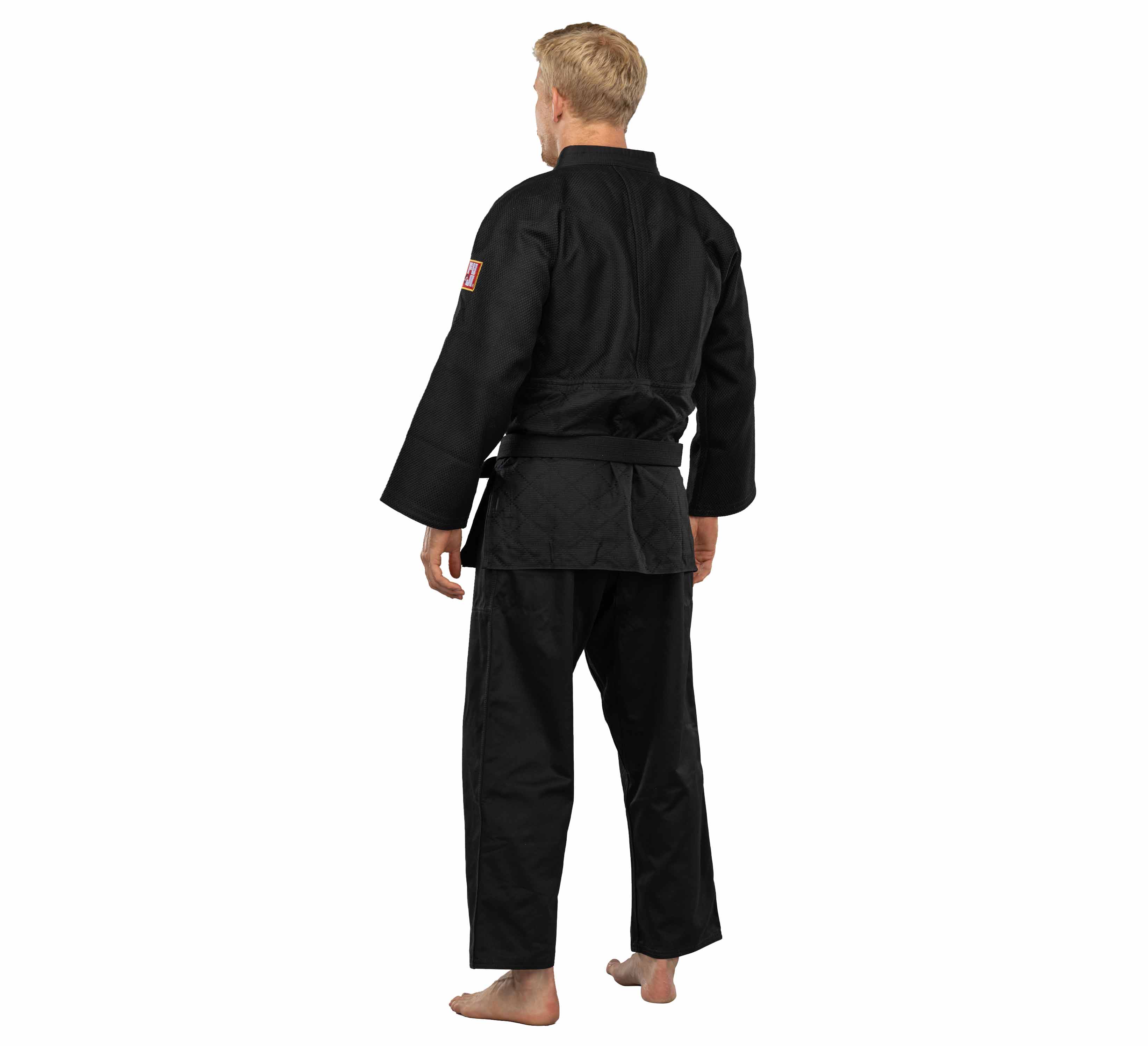 A barefoot blond man, seen from behind, stands on a white background wearing a black Euro Competition Judo Gi with a black belt.