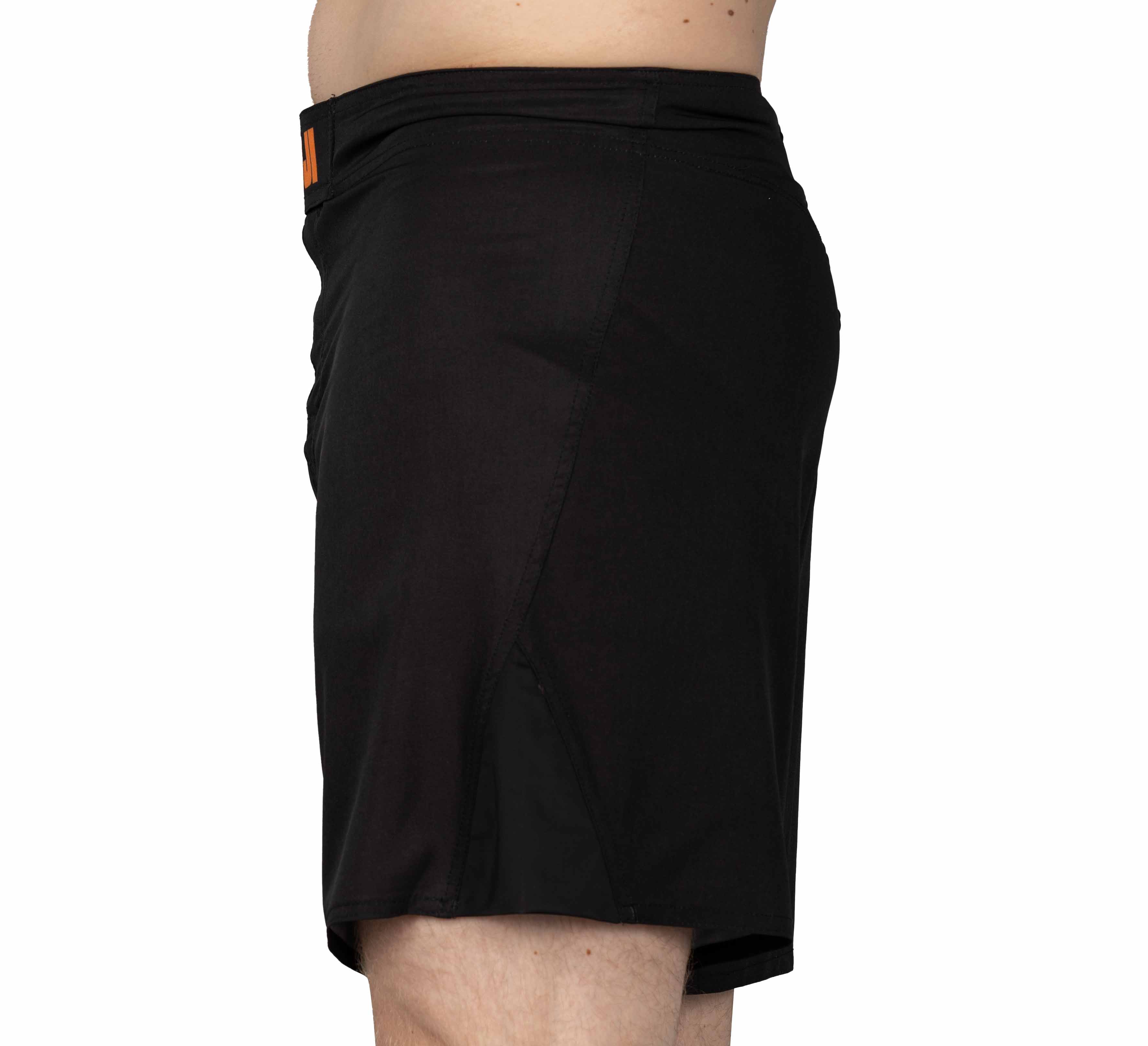 A model in profile wears Baseline Fight Shorts Black/Orange, shown from the waist to upper legs, posed against a plain white background.
