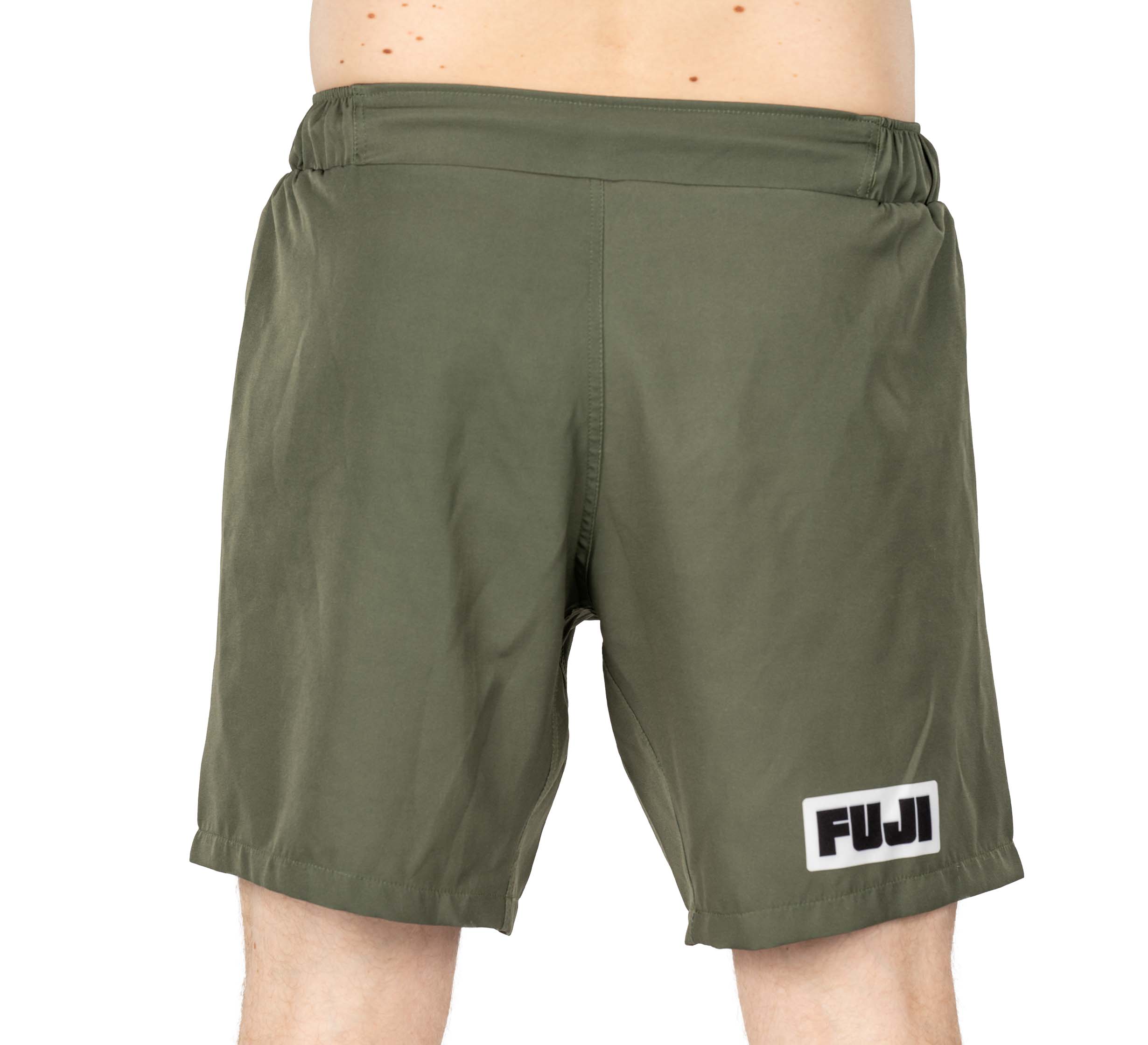 A person wearing Ultimate Grappling Shorts Military Green featuring an elastic waistband and a FUJI logo patch near the left hem. The shorts are shown from the front, waist to knees.