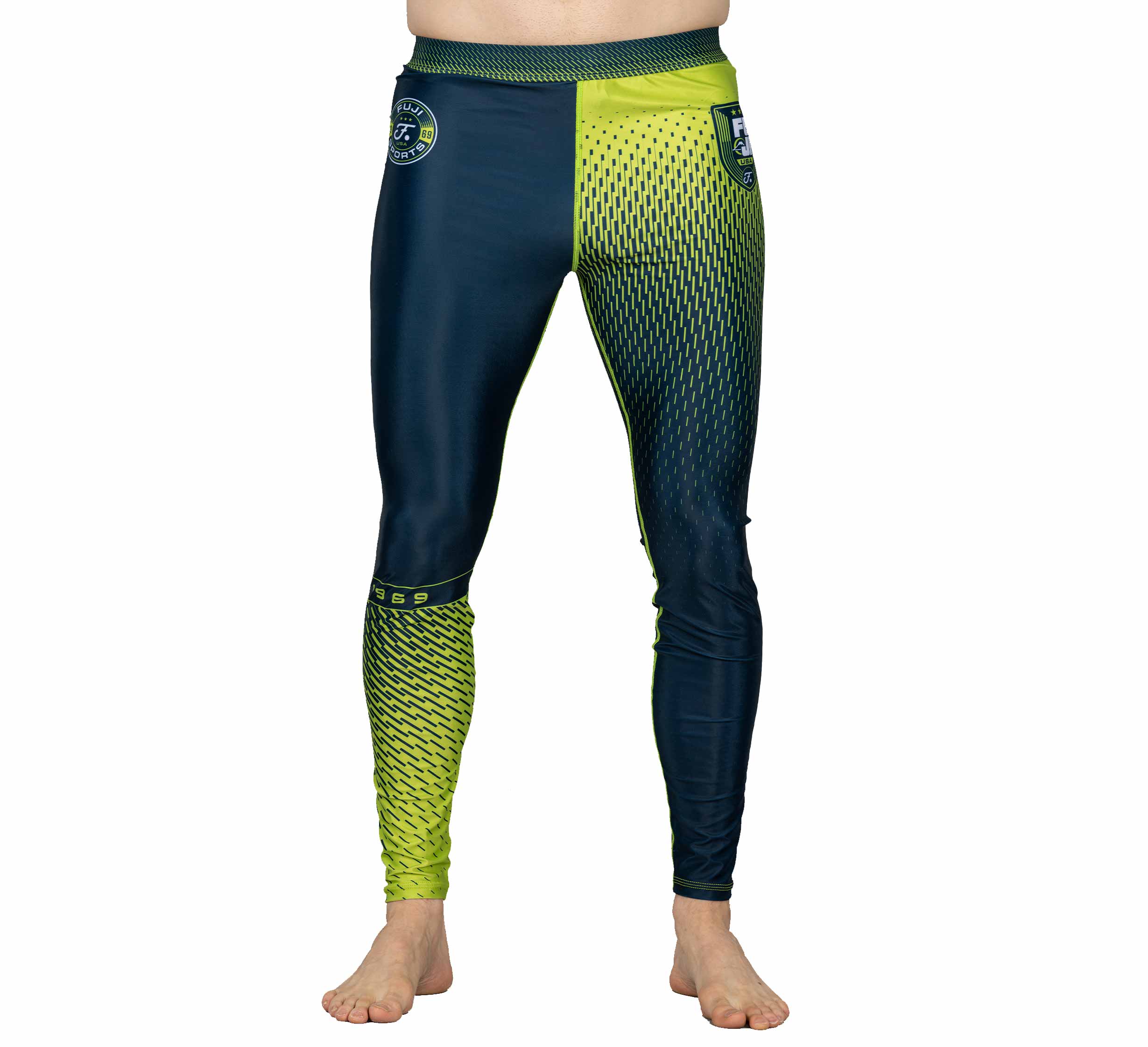 A person wearing Match Grappling Spats Navy—fitted, long athletic leggings with a blue and neon yellow geometric pattern, contrasting color design, and logo on the left hip—stands barefoot on a white background.