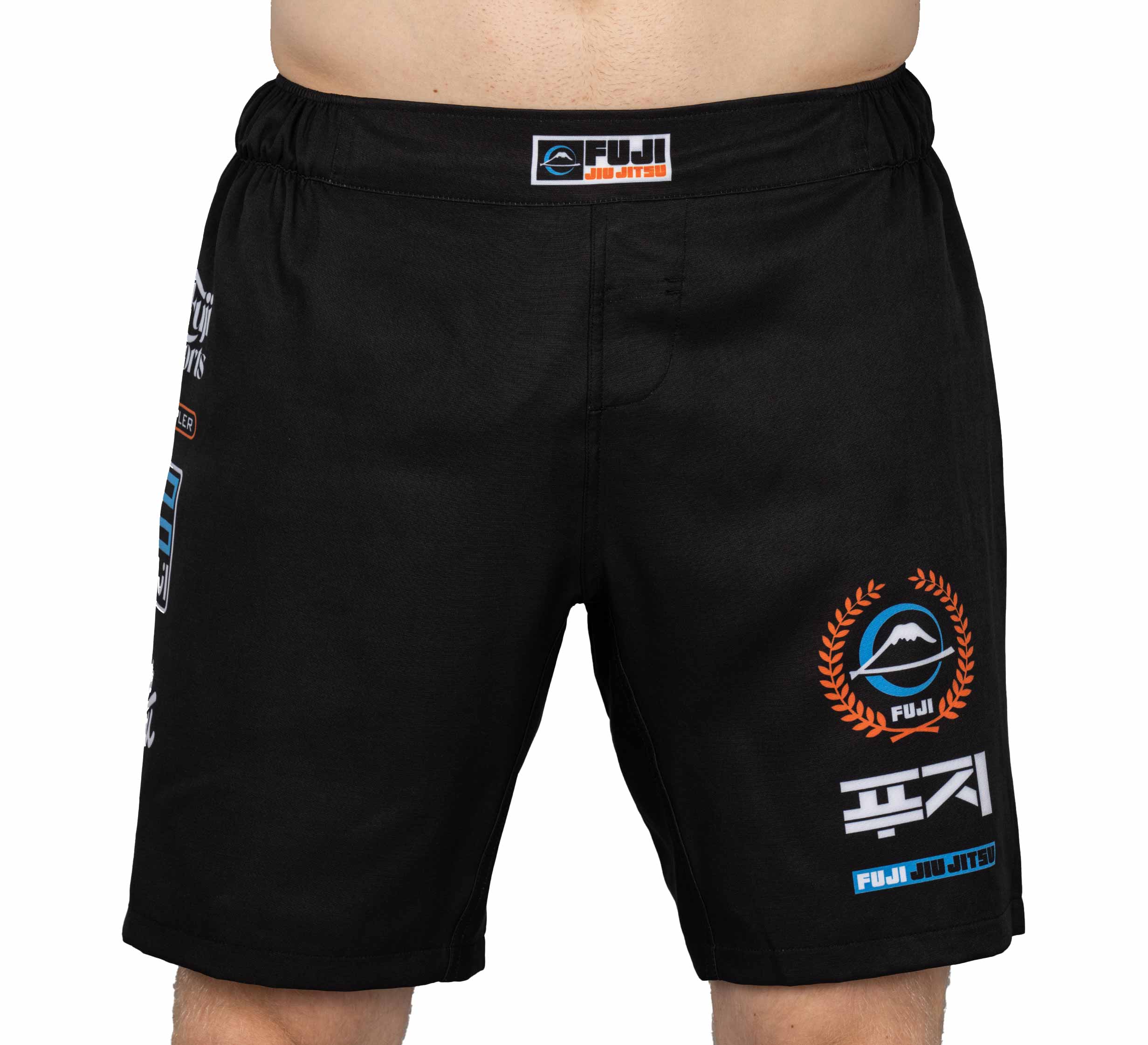 Someone wearing black XTR Extreme Grappling Fight Shorts, which display various white, blue, and orange logos and designs. The image shows only the lower torso and upper legs against a plain backdrop.
