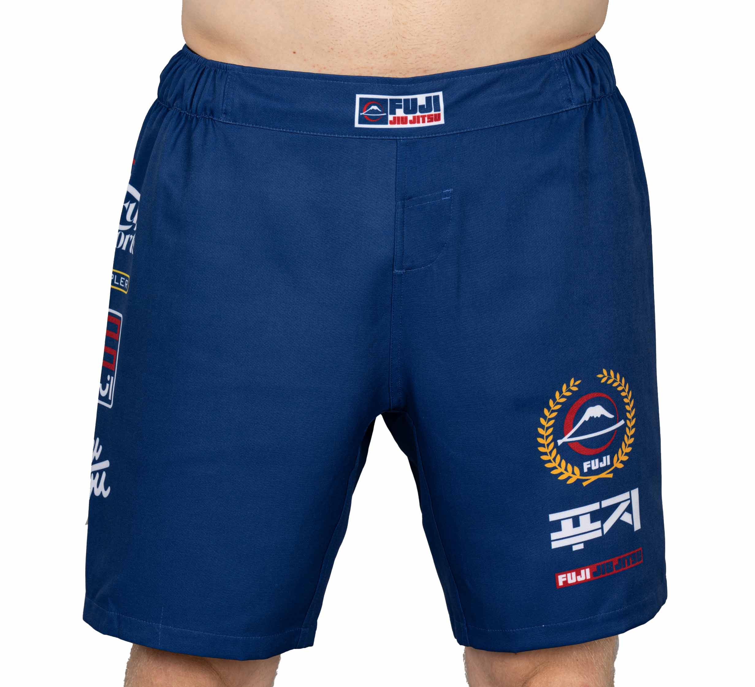 A person wearing FUJI XTR Extreme Grappling Fight Shorts in navy with white, red, and gold logos and designs, shown from waist to mid-thigh.