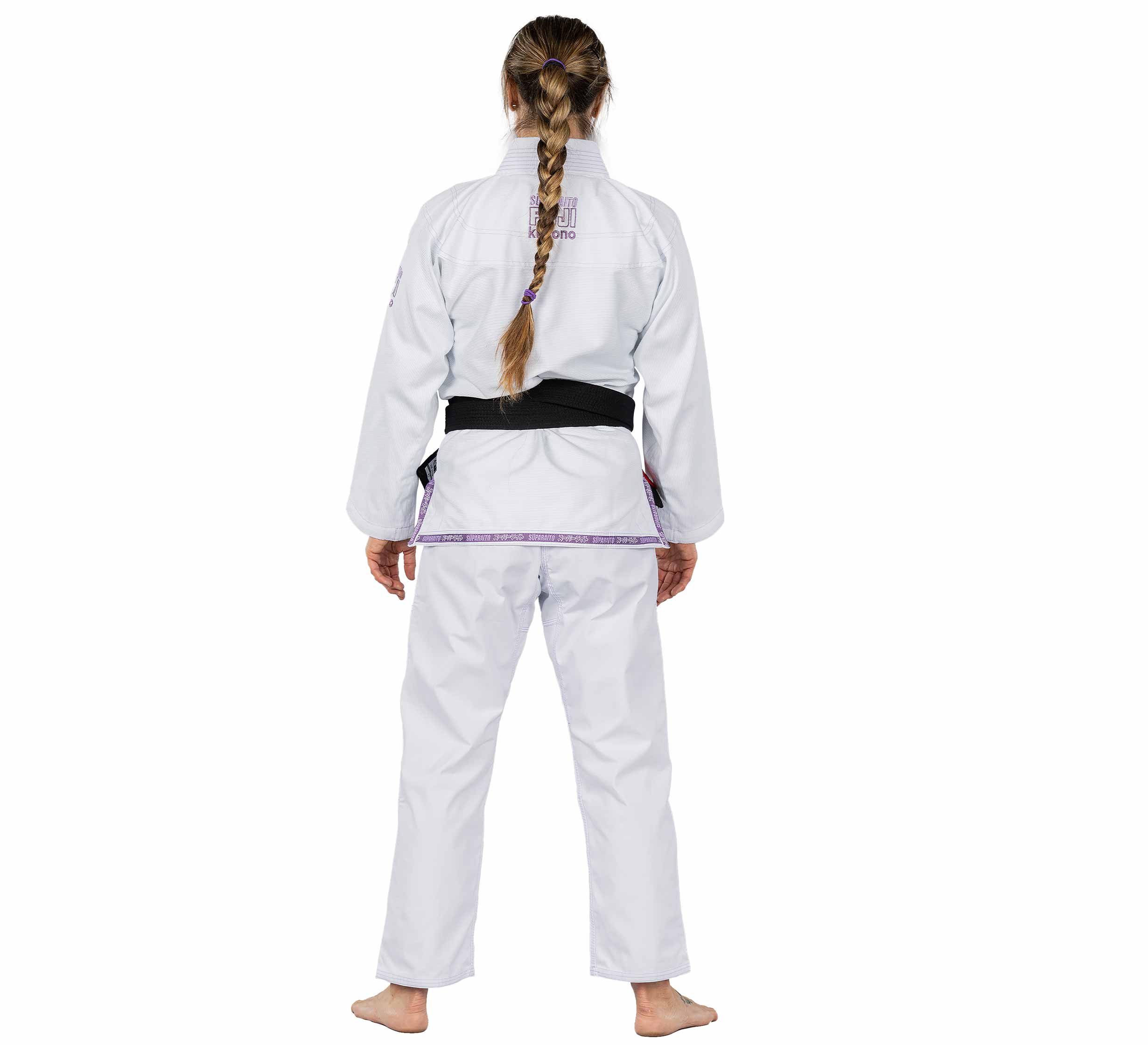 A person with braided hair, barefoot and facing away on a white background, wears the Suparaito Womens BJJ Gi in purple with a black belt.