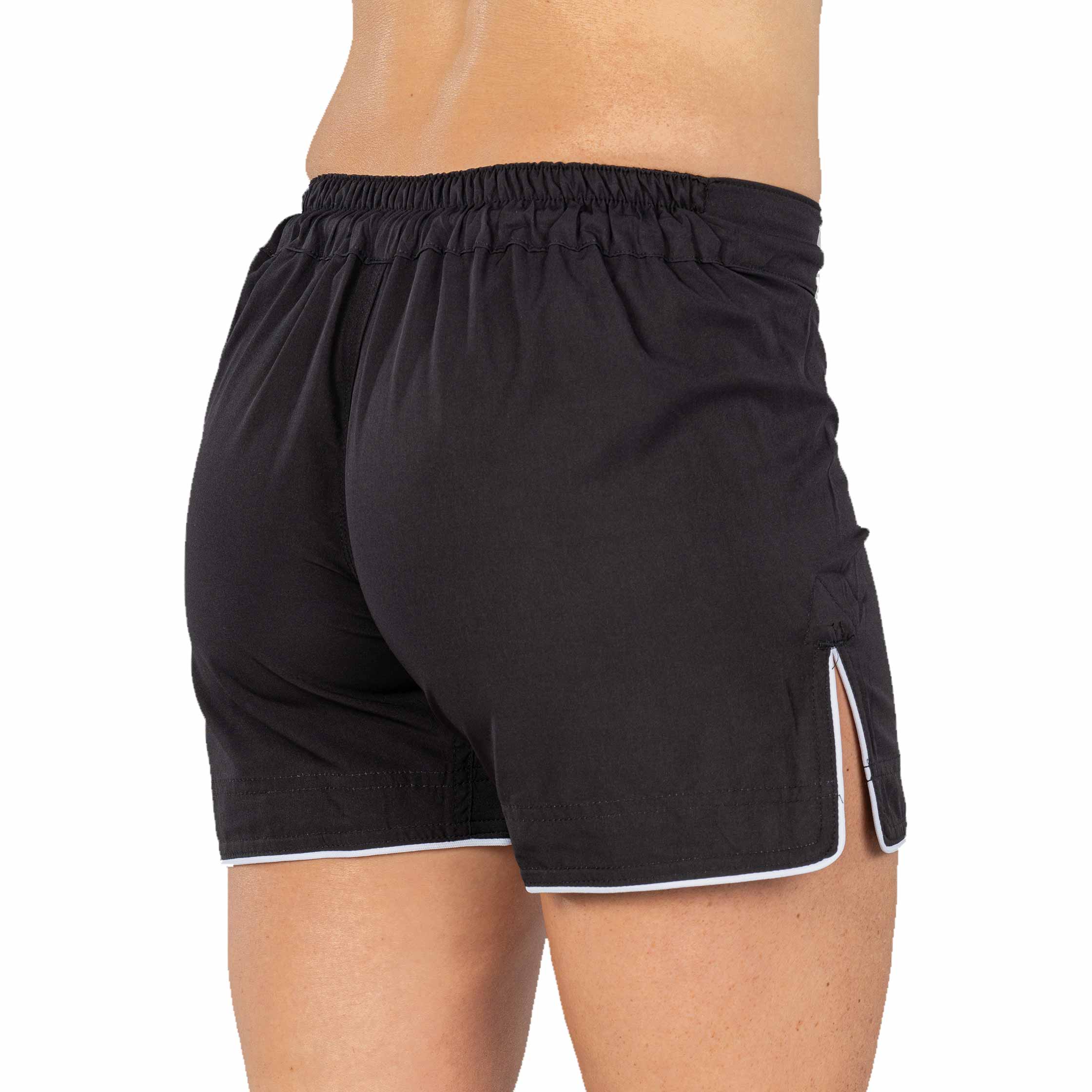 A person is shown from the back wearing Baseline Womens Black Grappling Shorts, featuring white trim, an elastic waistband, and a small side slit. The background is white.
