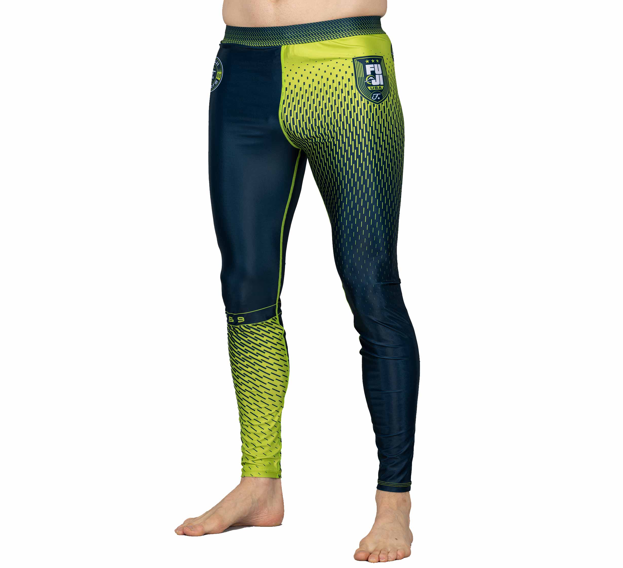 A person wears Match Grappling Spats Navy—tight-fitting athletic leggings with a blue and yellow gradient, geometric designs, and a small left hip logo—standing barefoot on a white background.