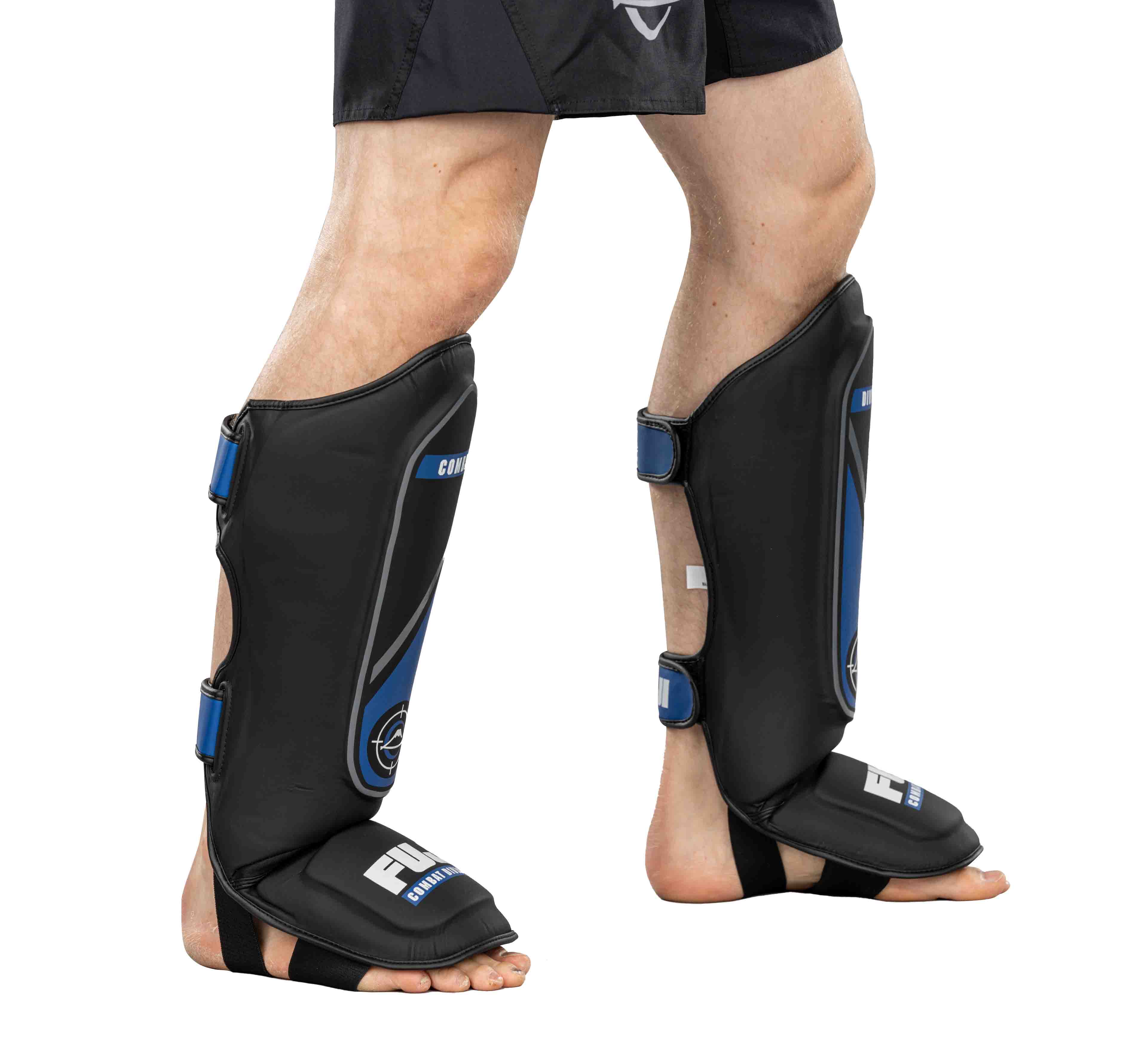 A person stands on a white background wearing Precision Striking Shin Guards in black and blue, featuring Velcro straps for secure fit and extended coverage over the front of the lower legs and feet, including foot protection straps.