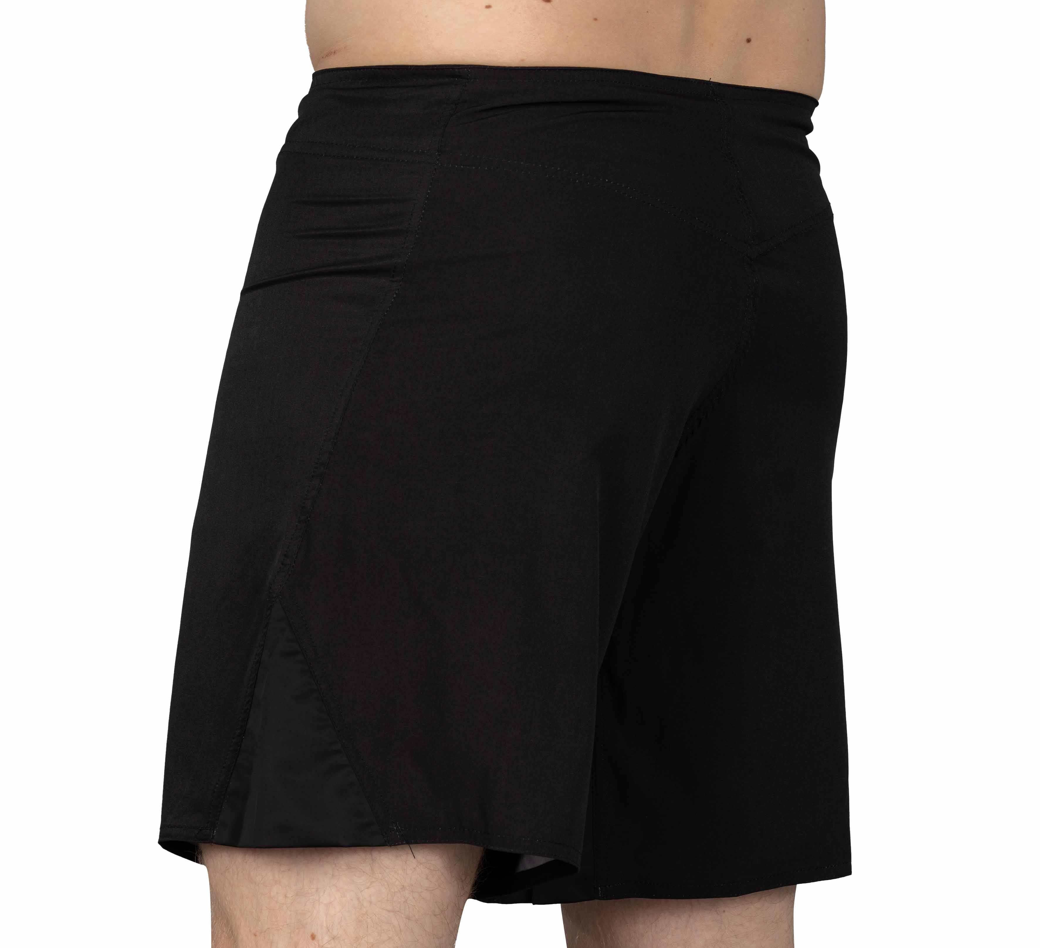 A person is shown from the waist down wearing Baseline Fight Shorts Black/Orange, with the image focusing on the back and side to highlight their fit and length.