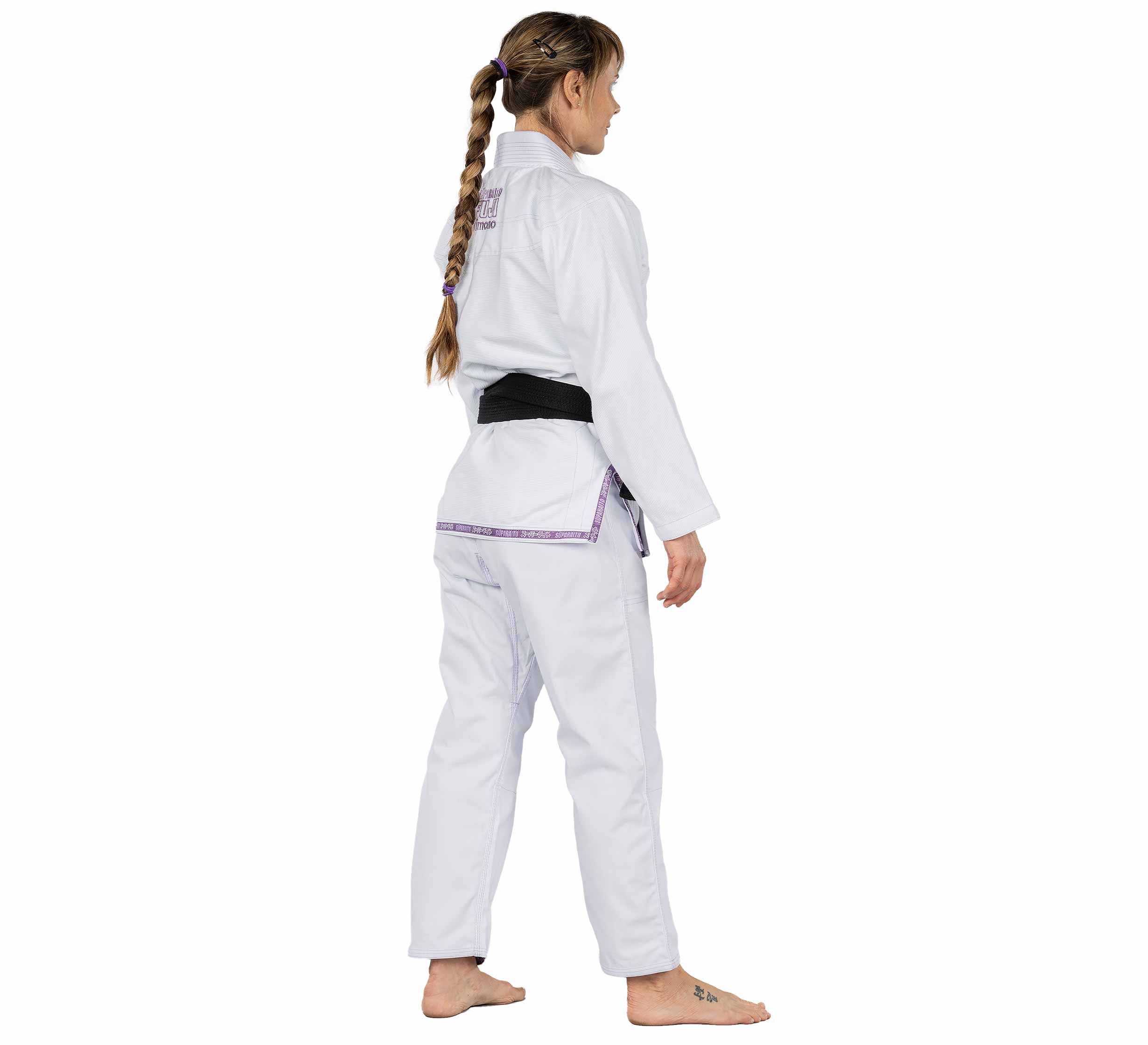 A woman with a long braid, barefoot and facing sideways against a white background, wears the Suparaito Womens BJJ Gi in purple with a black belt.