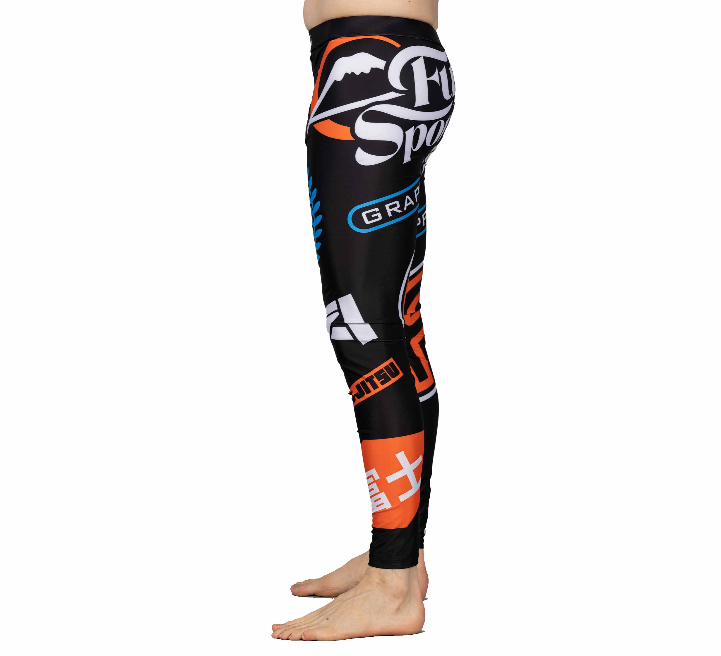 A person stands barefoot in profile, wearing XTR Extreme V1 Grappling Spats Black, which feature colorful logos and text in orange, white, and blue designs.