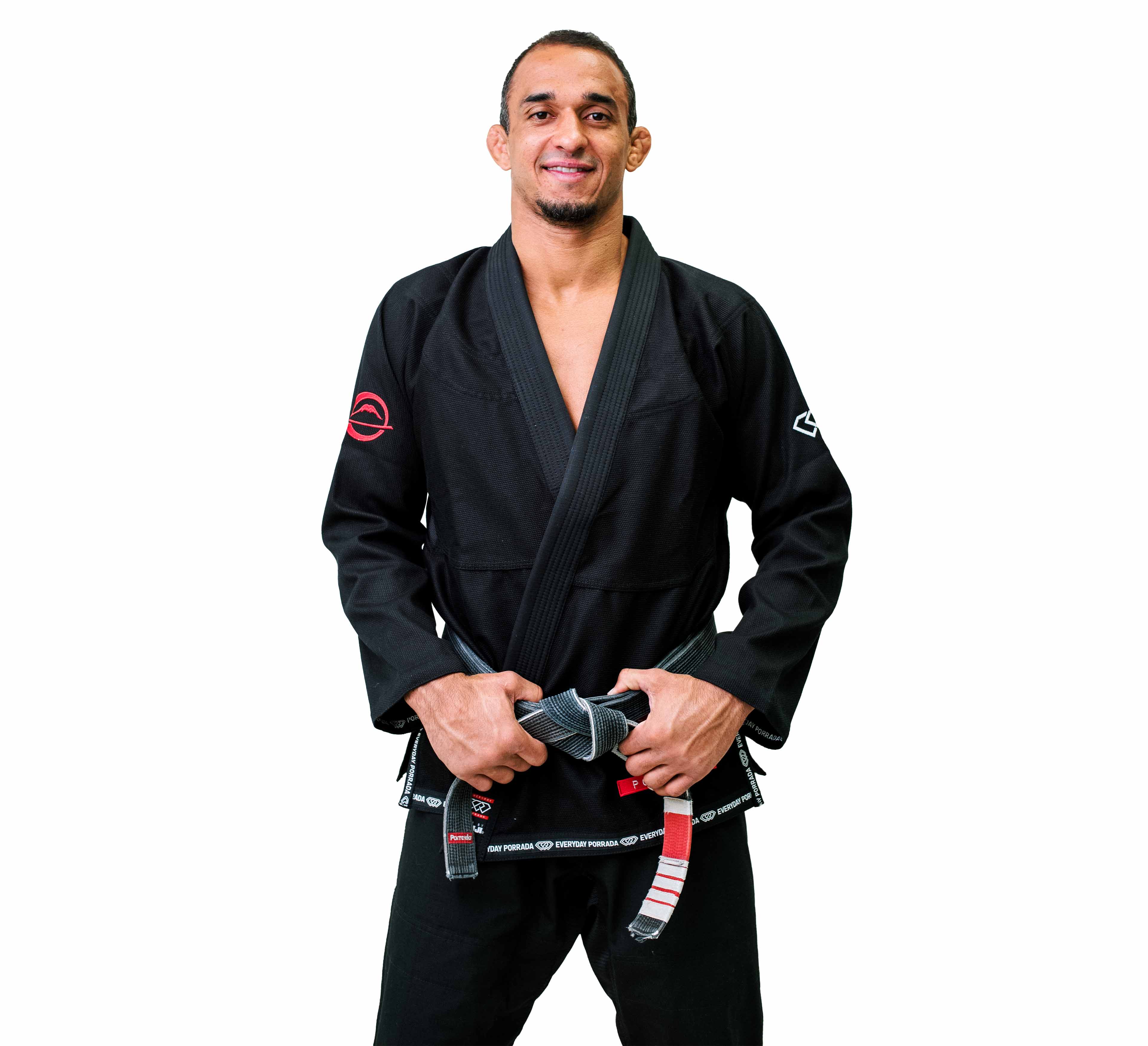 A man wearing the Everyday Porrada Flow-Tech BJJ Gi smiles while holding a black belt with red and white stripes in front of him against a plain white background.